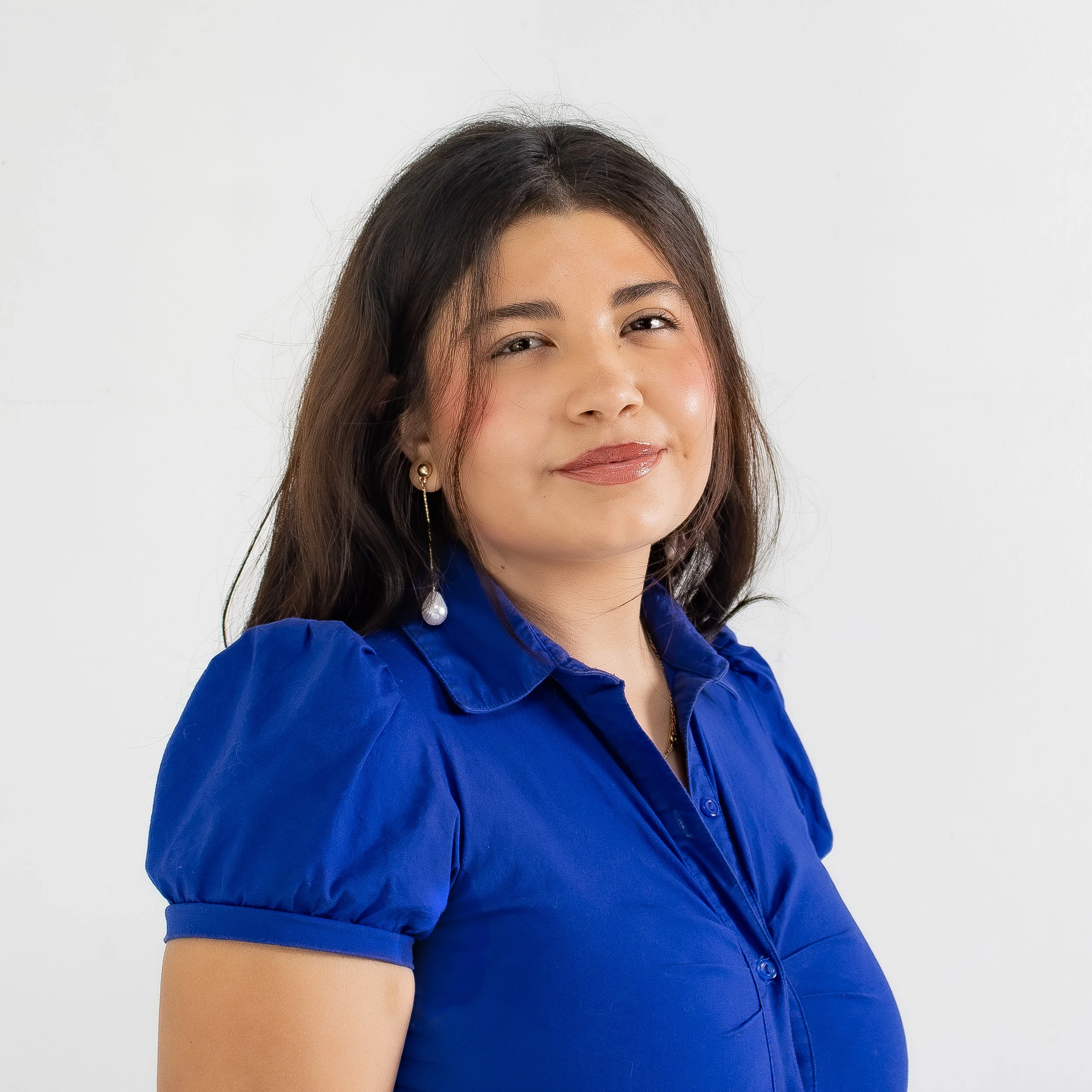 Close-up of a woman with long dark hair, wearing a bright blue jacket with puffed sleeves, standing against a plain white background.