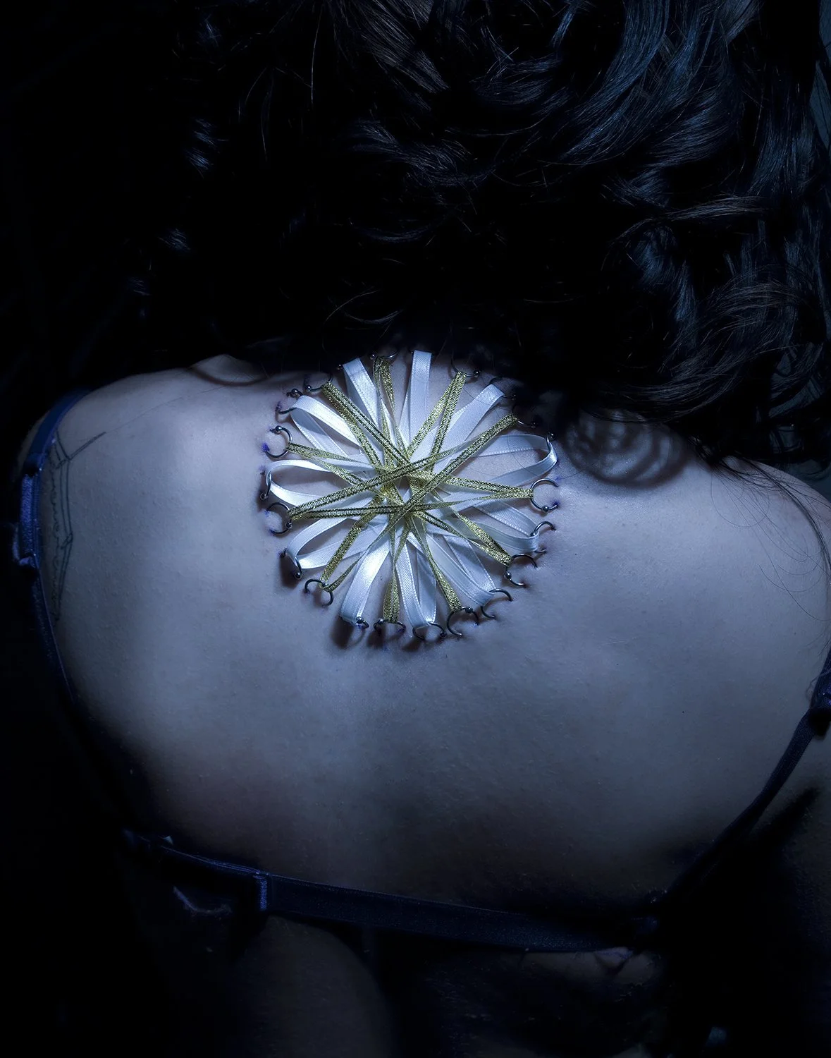Close-up of a corset piercing made of various ribbons arranged in a radial pattern on the upper back.