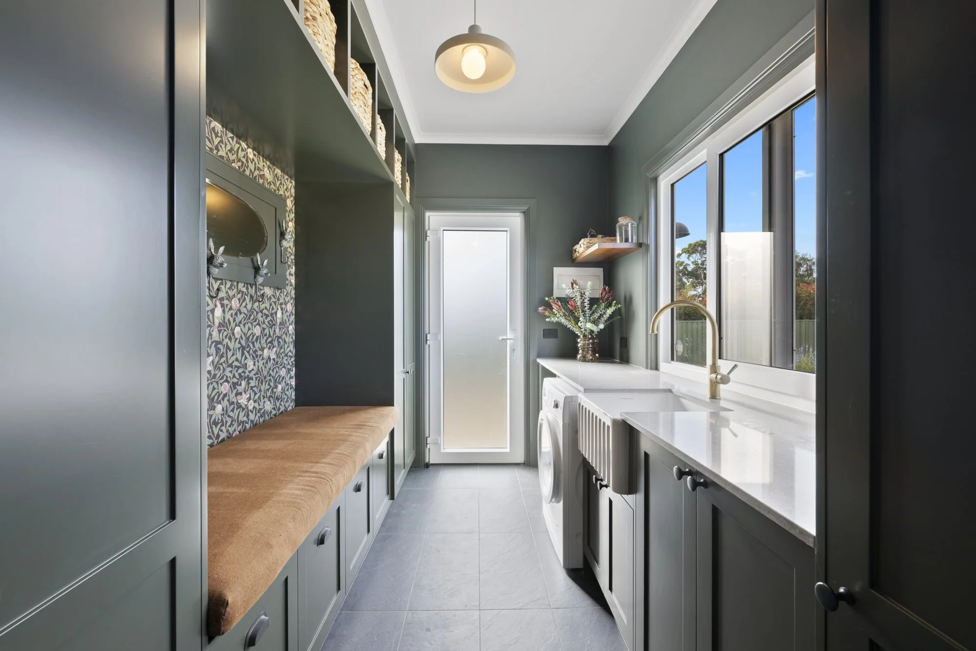 Bright laundry room with dark green cabinetry, white countertops, large window, washing machine, and door at the end.