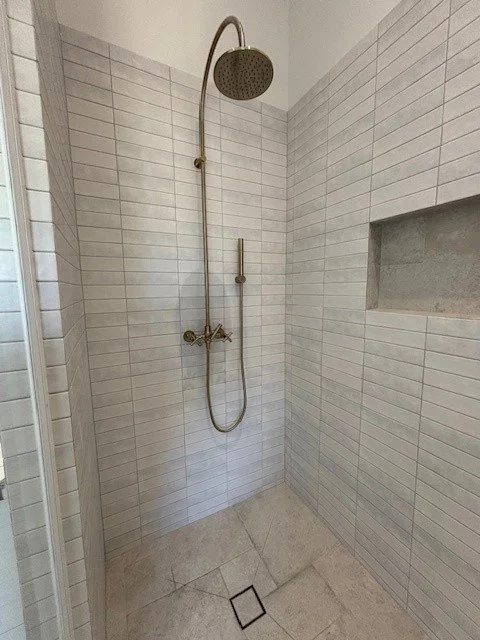 Bathroom shower with a rain showerhead, wall-mounted handheld shower, and a built-in niche for toiletries.