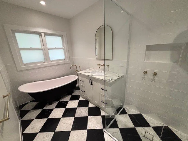 Bathroom with black and white checkered floor, clawfoot bathtub, white vanity with a mirror, and a glass-enclosed shower.