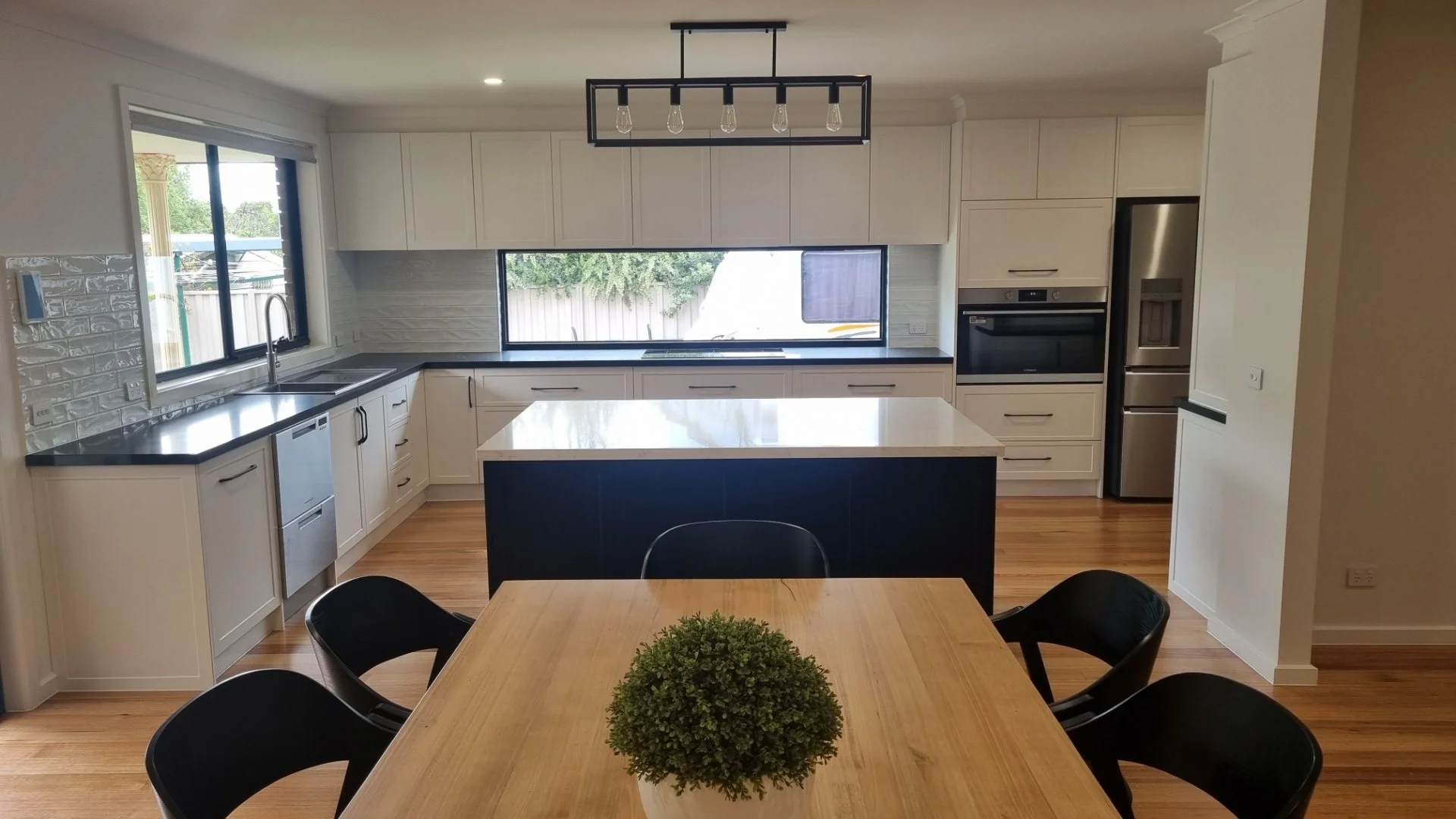 Modern kitchen with white cabinets, black countertops, a kitchen island, and a dining table with black chairs and a green plant centerpiece.