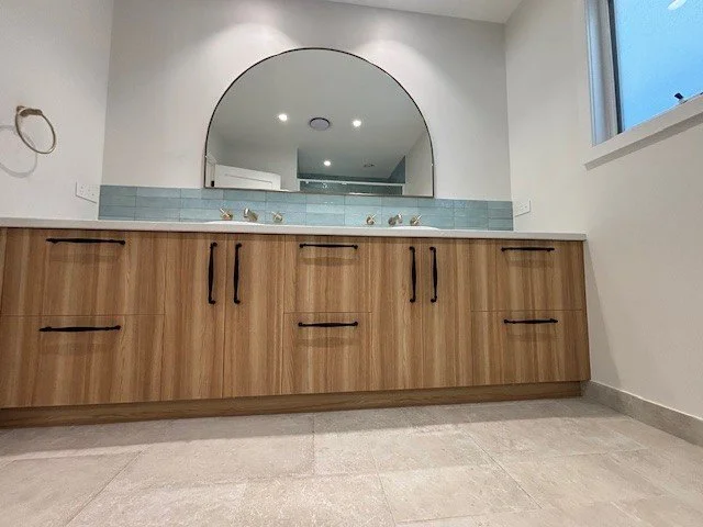 Bathroom with a wooden vanity, a large arched mirror, a light blue tiled backsplash, and a window on the right side.