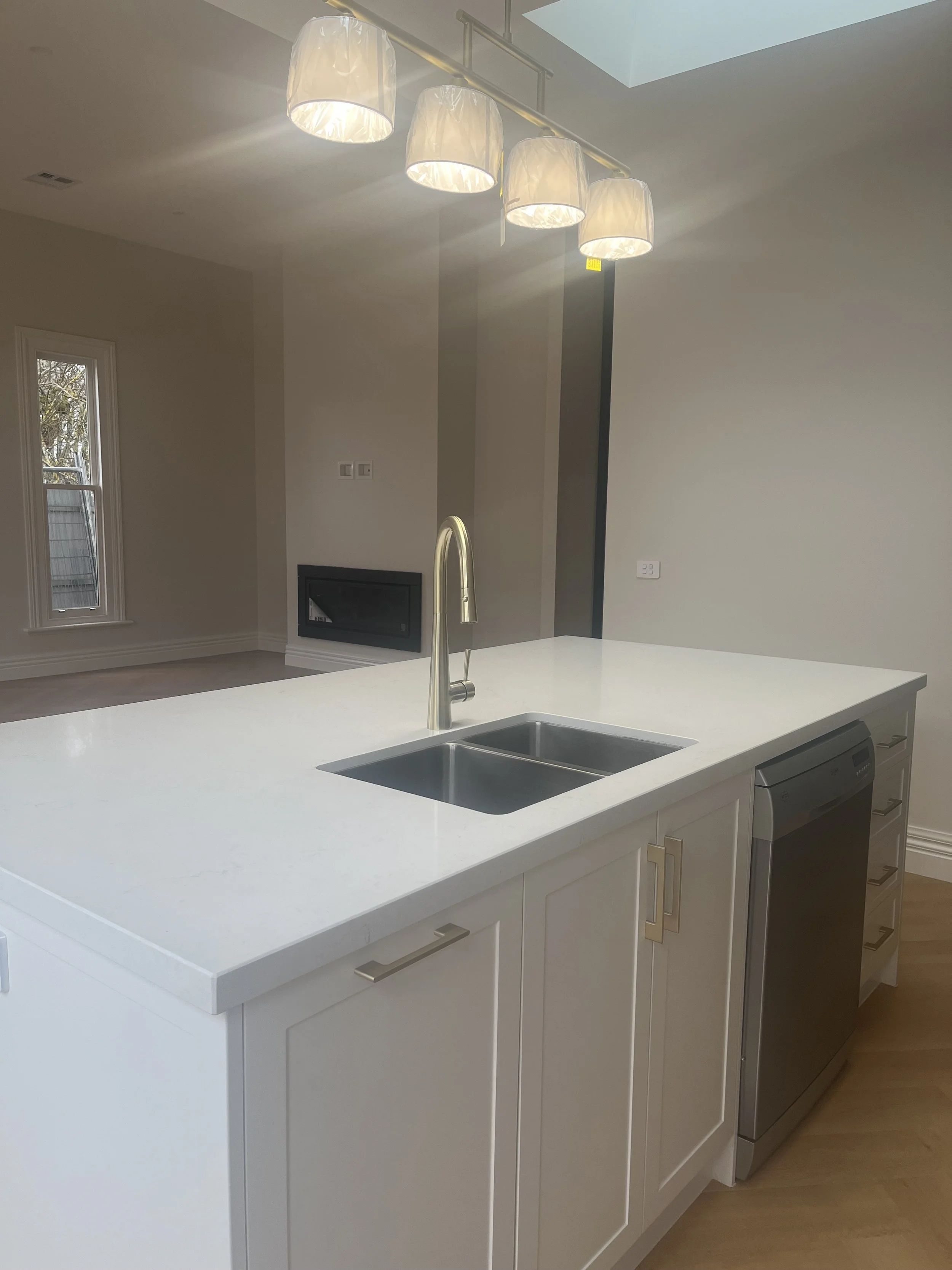 Modern kitchen with white island counter, stainless steel sink, and hanging pendant lights.