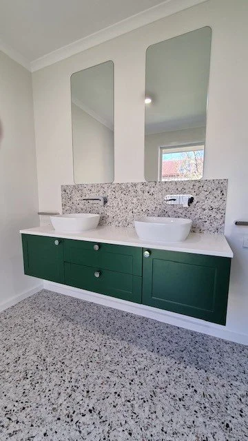 Modern bathroom vanity with two vessel sinks, green cabinet, granite countertop, and two tall mirrors on the wall.