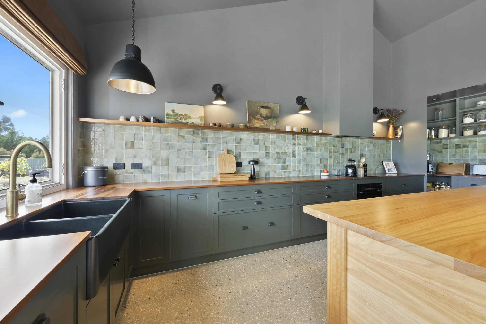 Modern kitchen with green cabinetry, wooden countertops, a black sink, and a window showing a garden view.