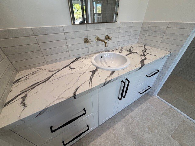 Bathroom vanity with a marble countertop, white sink, gold faucet, and black handles on drawers and cabinets.