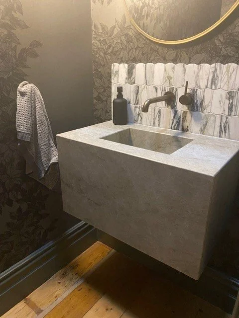 A modern bathroom sink with a marble wall and a round mirror above, with a soap dispenser and towel on the side.
