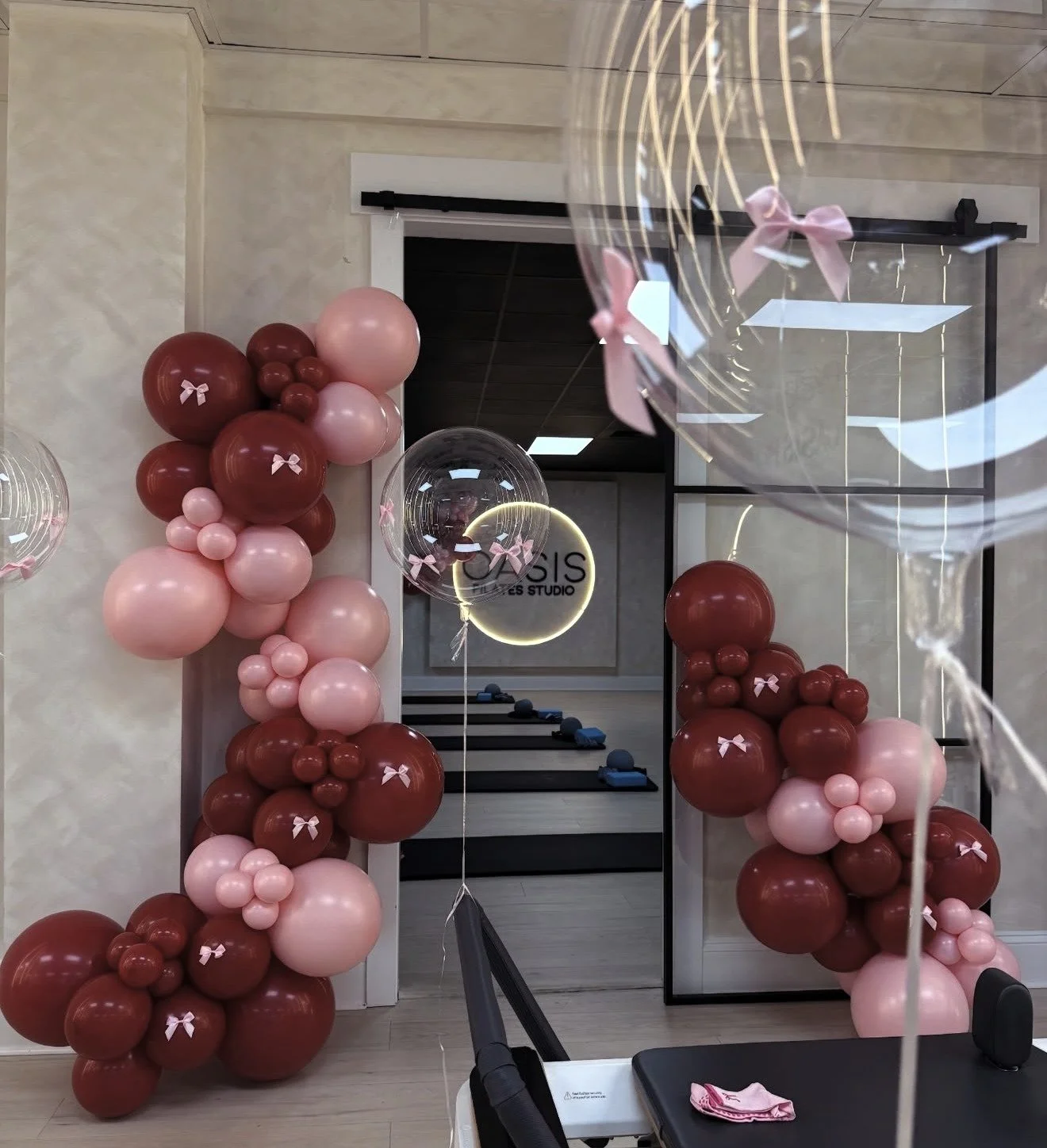 Decorative balloon arch made of pink and maroon balloons with small pink bows in an event space.