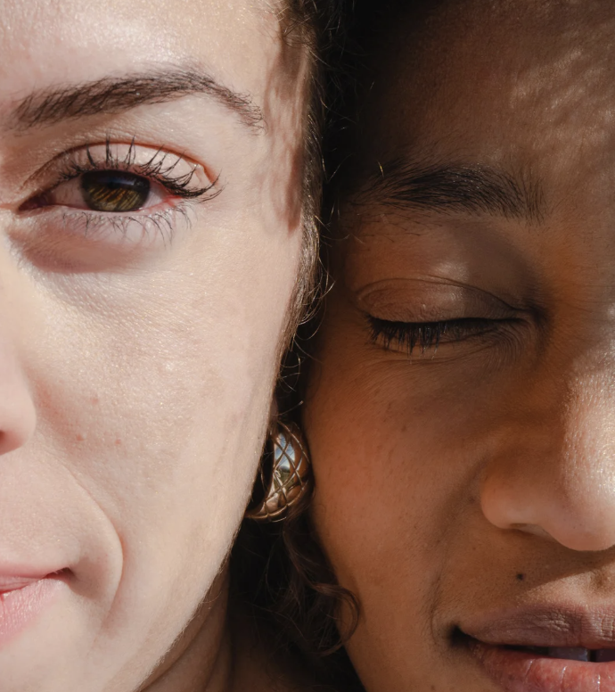 Close-up of two people with their faces very close together, one with light skin, the other with darker skin, both with closed eyes.