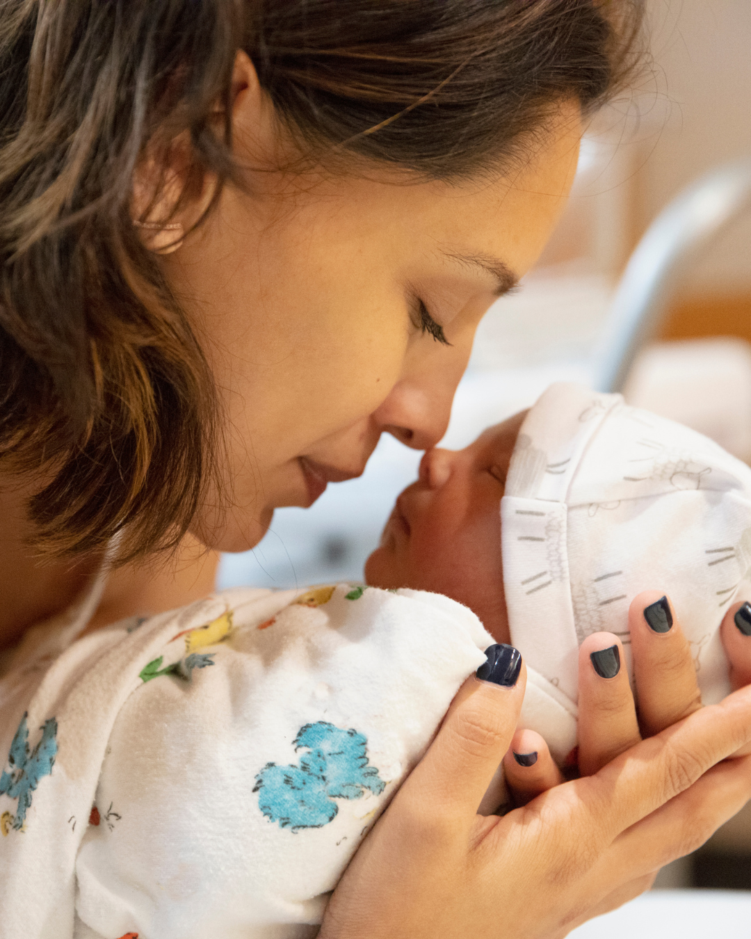 A woman holding a newborn baby close, touching noses, both with their eyes closed in an intimate moment.