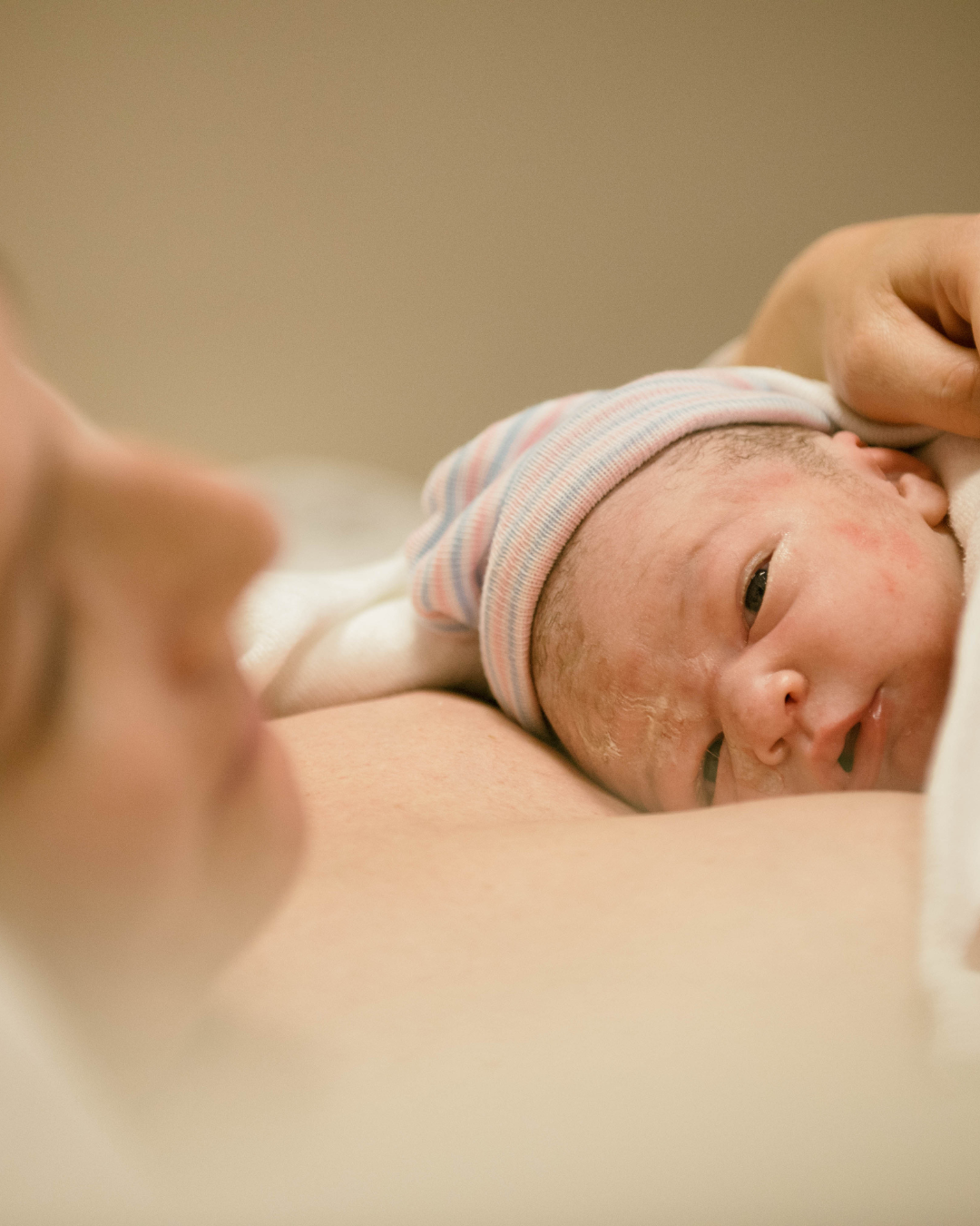 Newborn baby with a striped hat lying on mother’s chest.