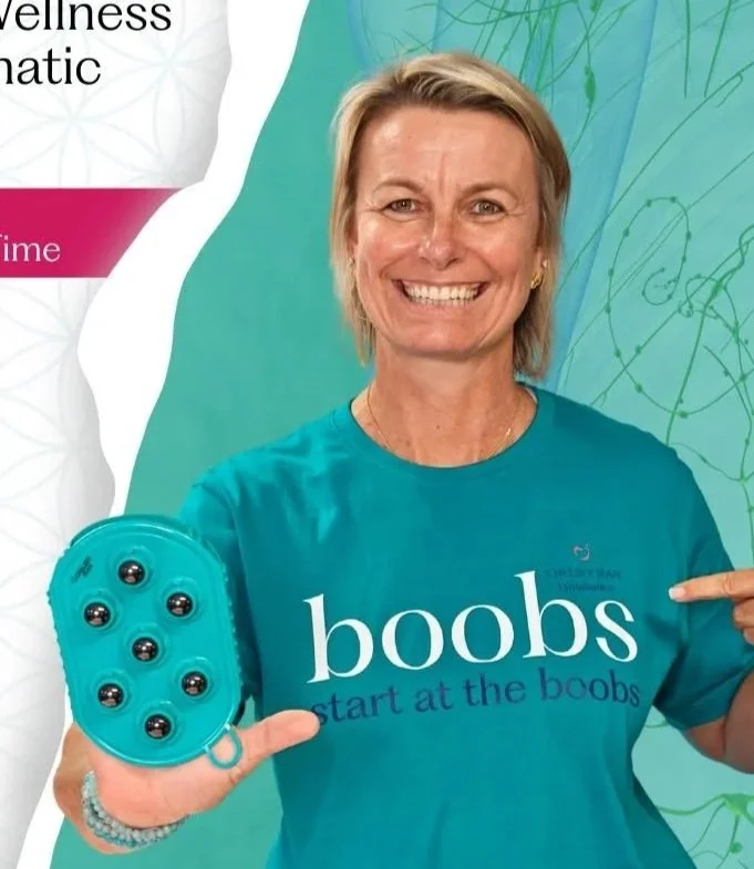 A smiling woman with blonde hair holding a blue massage tool with six black nodes, pointing to her shirt that reads 'boobs start at the boobs' in front of a teal background.