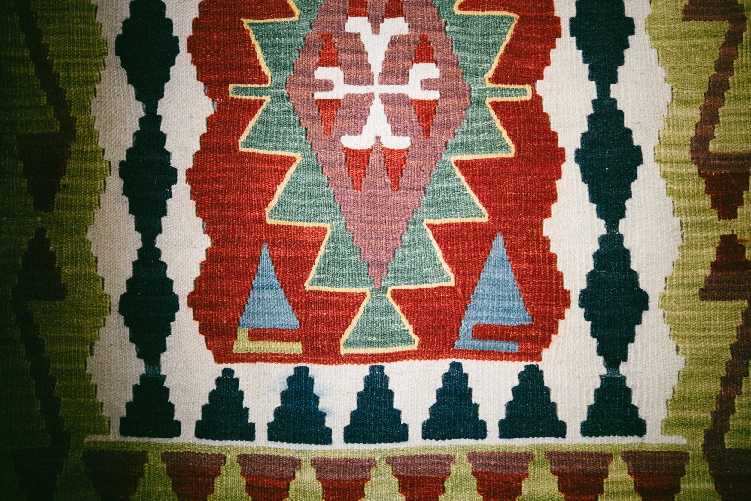 A colorful, patterned rug featuring geometric shapes and designs in red, green, blue, white, and brown colors.