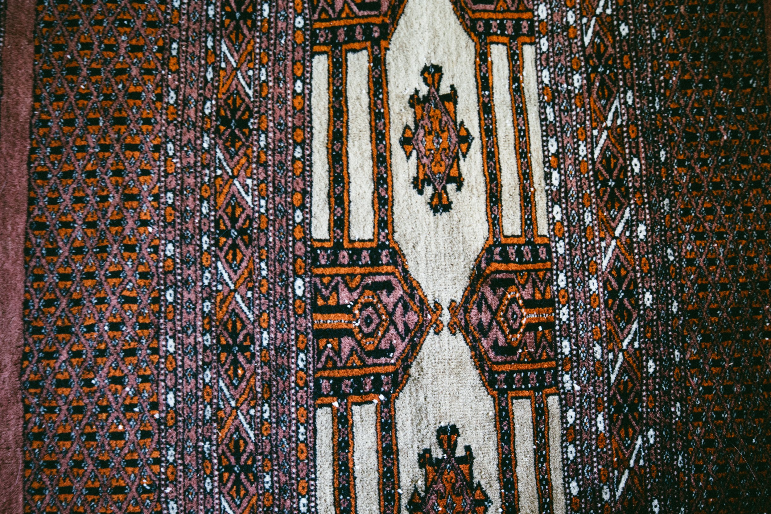 Close-up of a colorful, intricate Oriental carpet with geometric patterns in red, black, white, and purple.