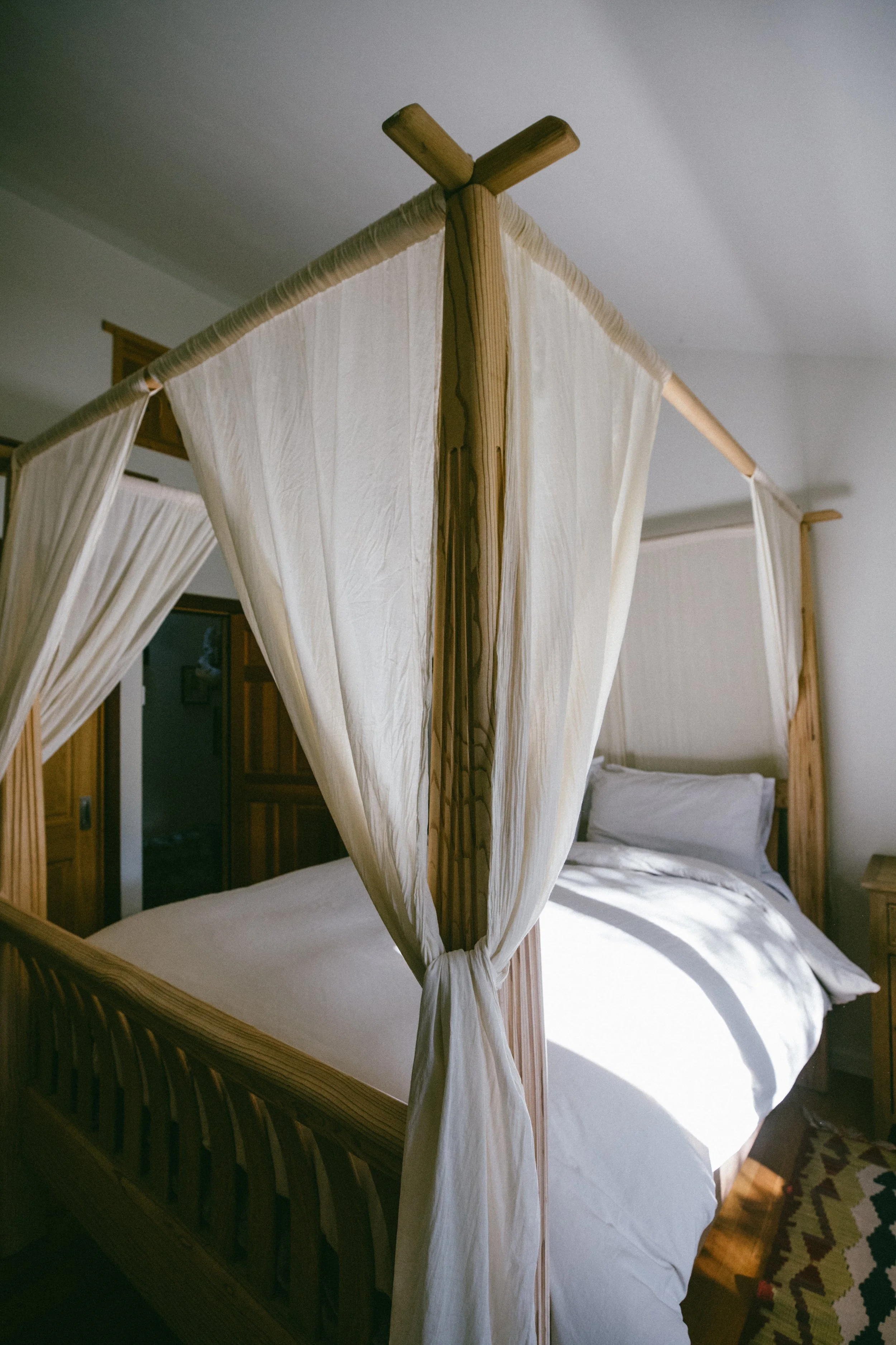 A wooden four-poster bed with white curtains in a cozy bedroom.