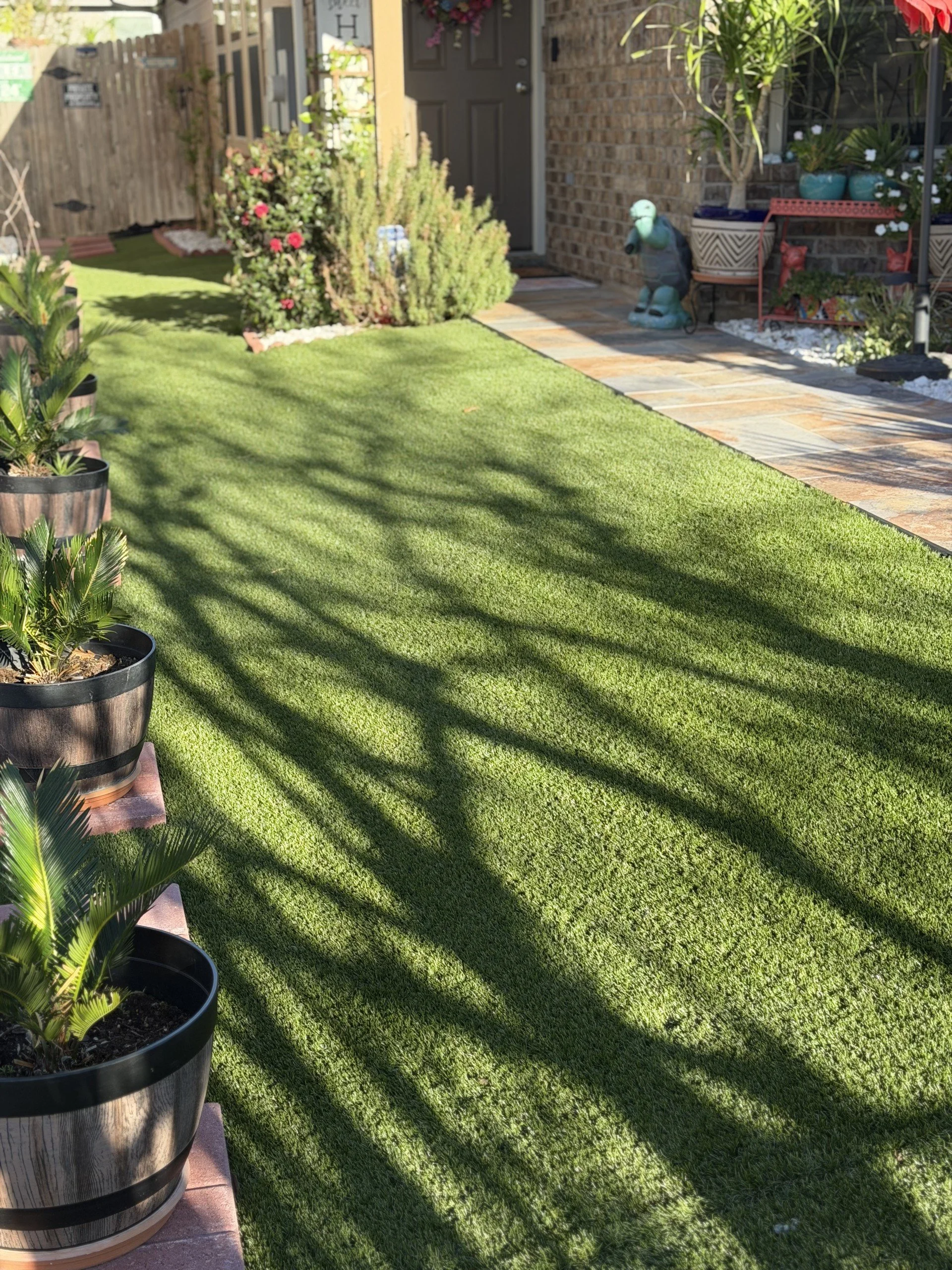 A backyard garden with potted plants, a grassy lawn, a brick and tile patio, and various decorative garden ornaments.