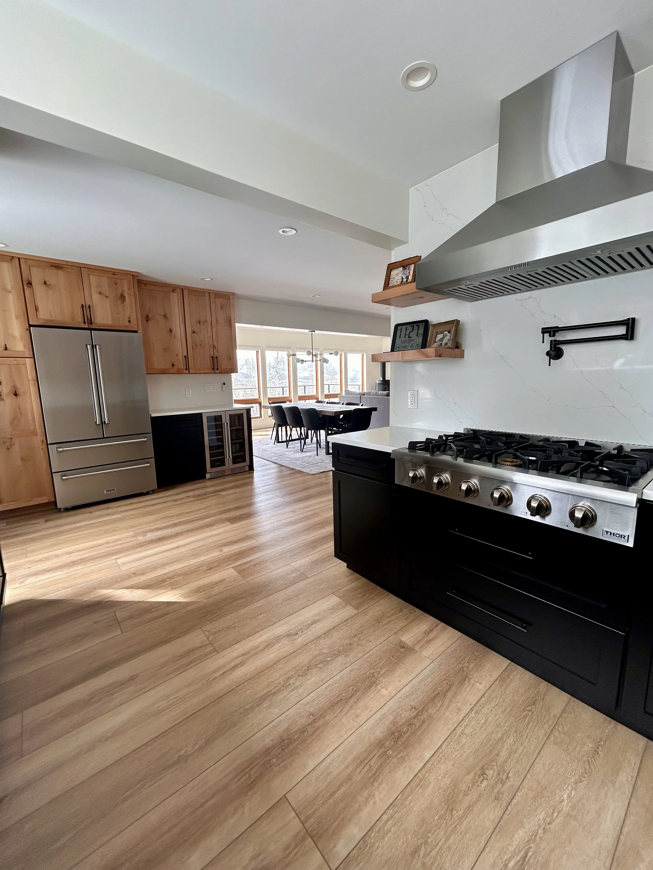 Modern mountain kitchen with wooden cabinets, stainless steel appliances, black and wood cabinetry, and a dining area with a table and chairs in the background.