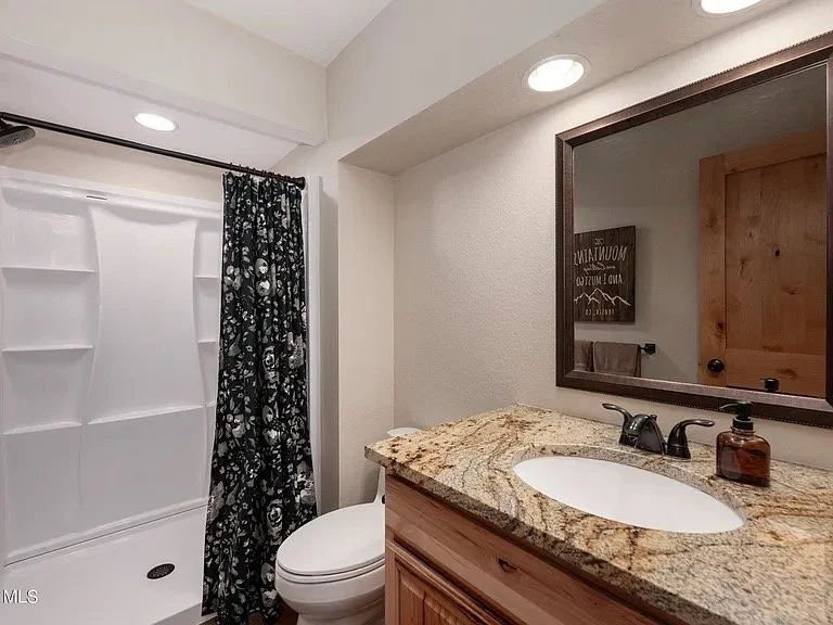 Bathroom with shower, toilet, wooden vanity with granite countertop, and mirror.