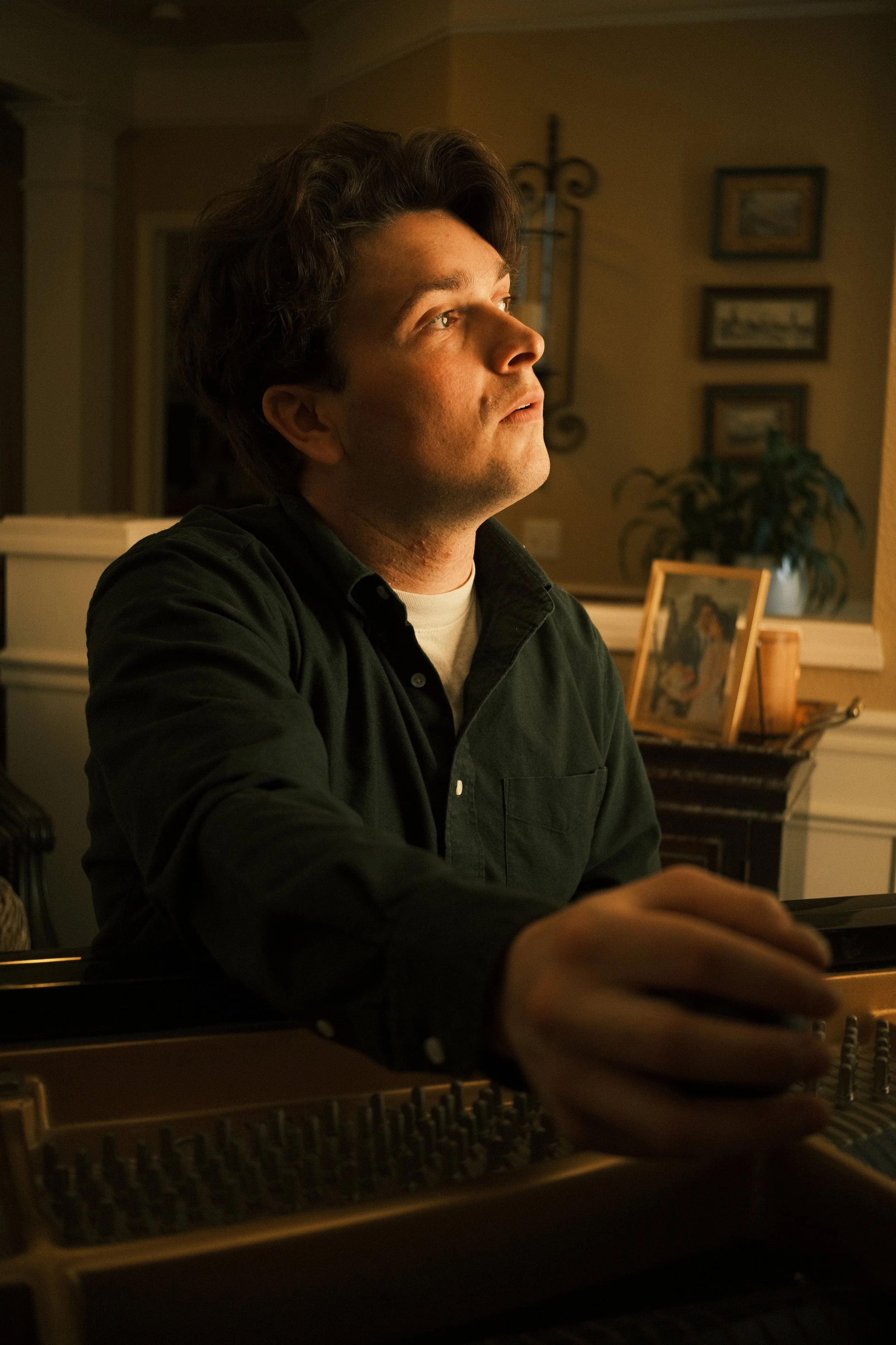 A man with dark, curly hair playing a keyboard in a warmly lit room.