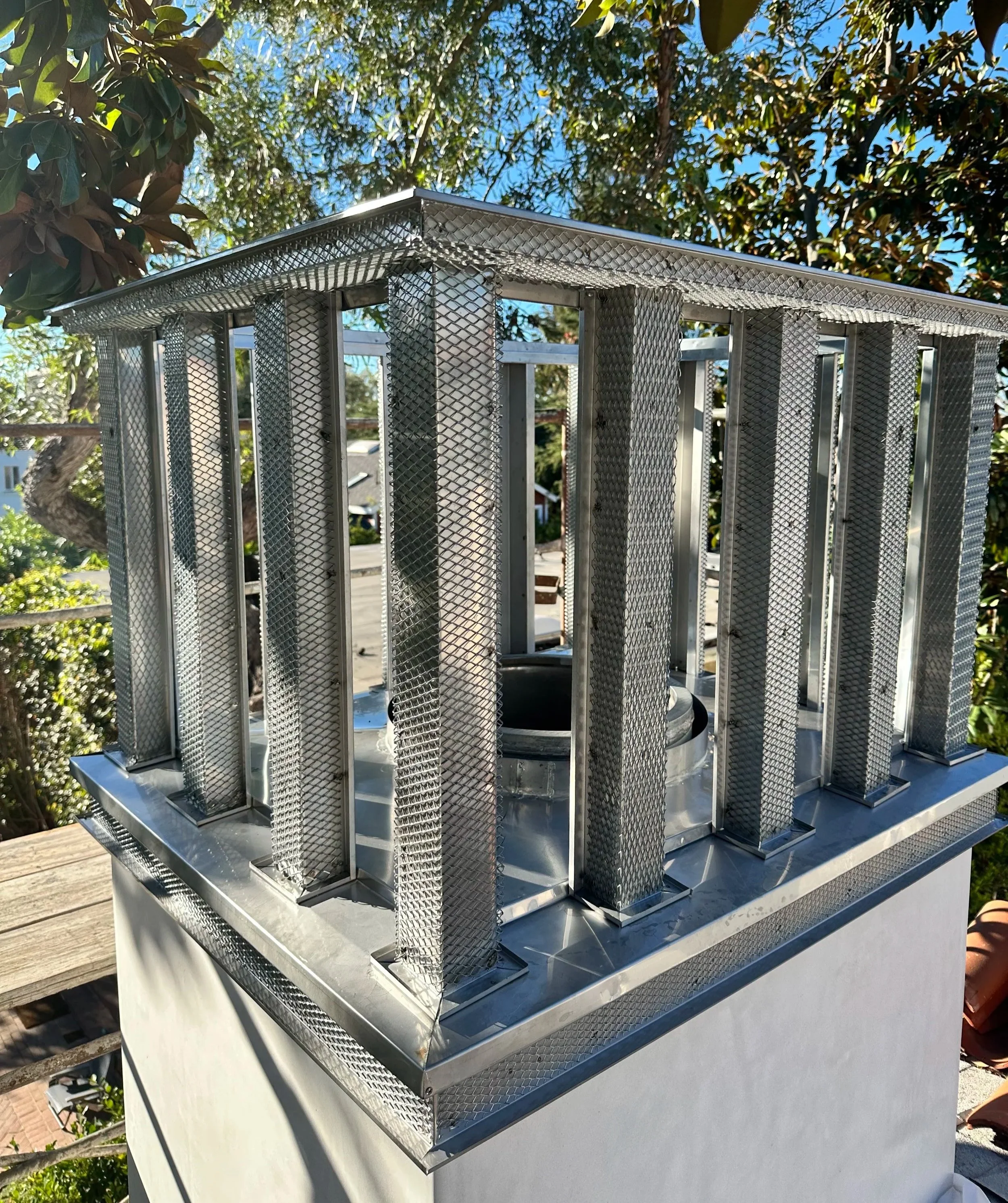 Metal outdoor air conditioning unit on a white wall with trees and blue sky in the background.