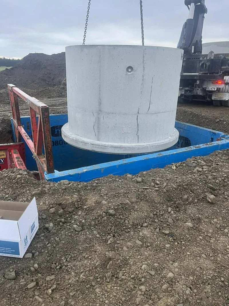 A large concrete structure is being lowered into a blue reinforced concrete form at a construction site. There is a crane and a truck in the background.