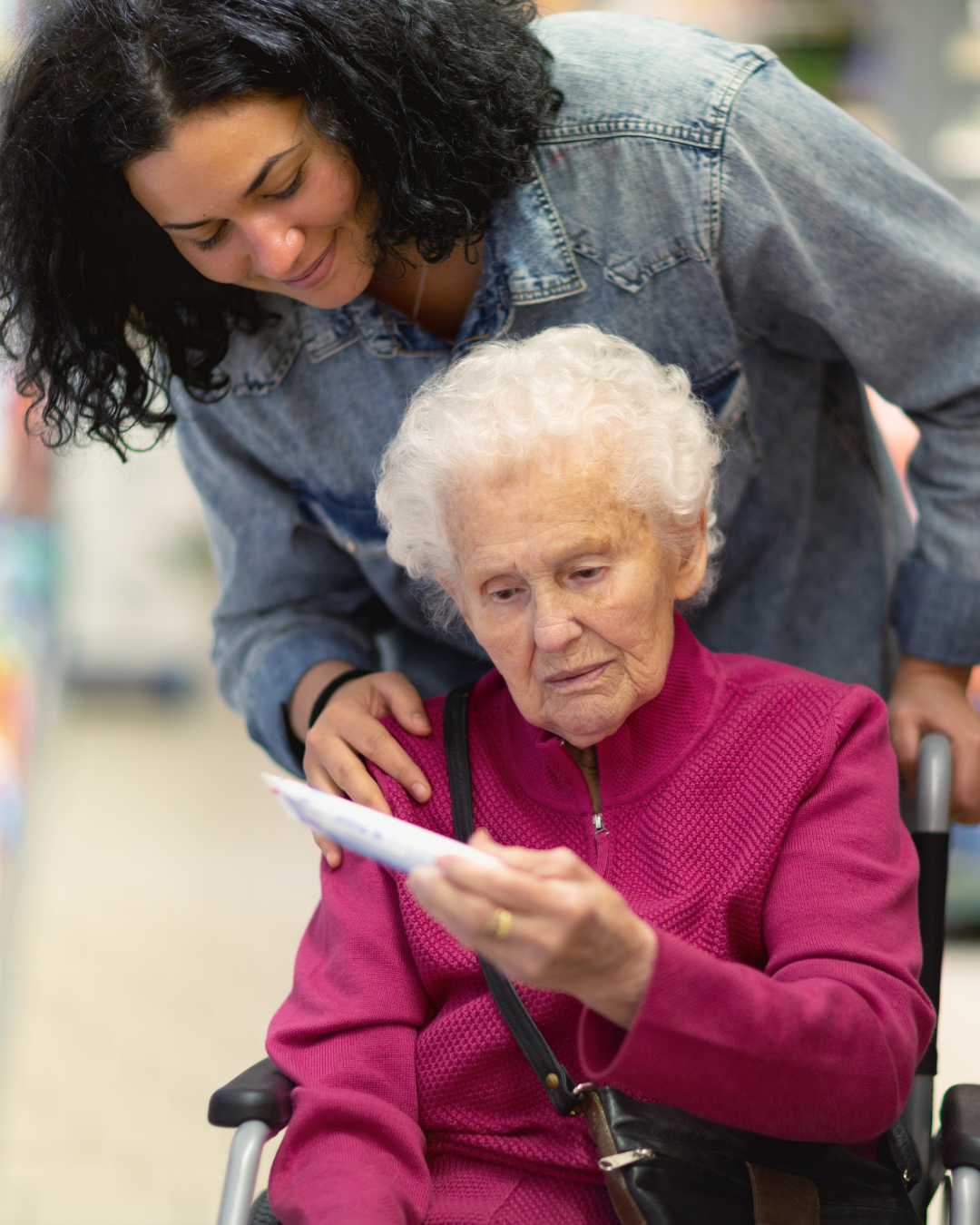 Young woman helping elderly woman in a wheelchair read a piece of paper in a store.