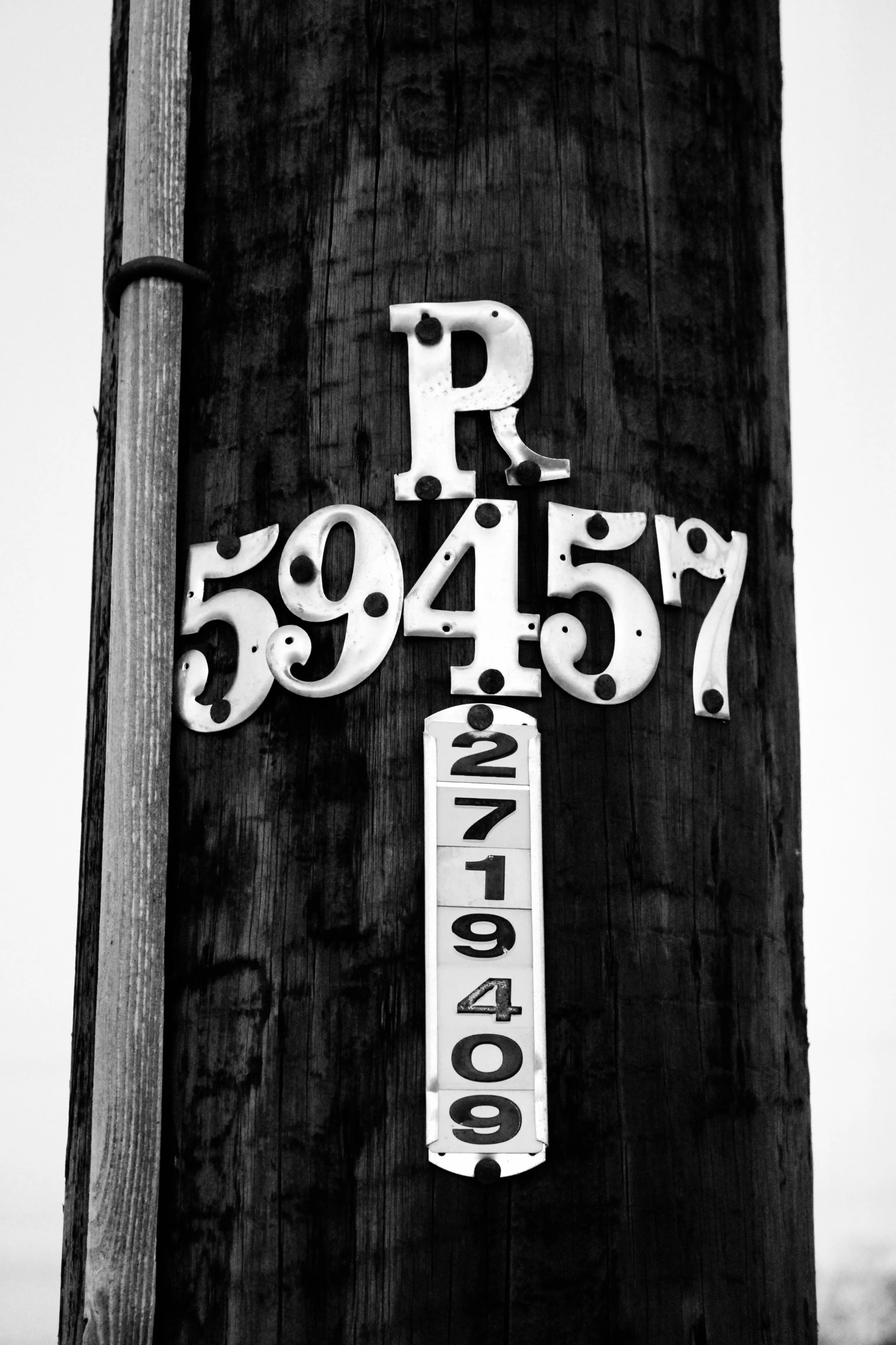 Close-up of a wooden utility pole with several mounted address signs displaying the numbers '59457' and '19409' in black on white backgrounds.