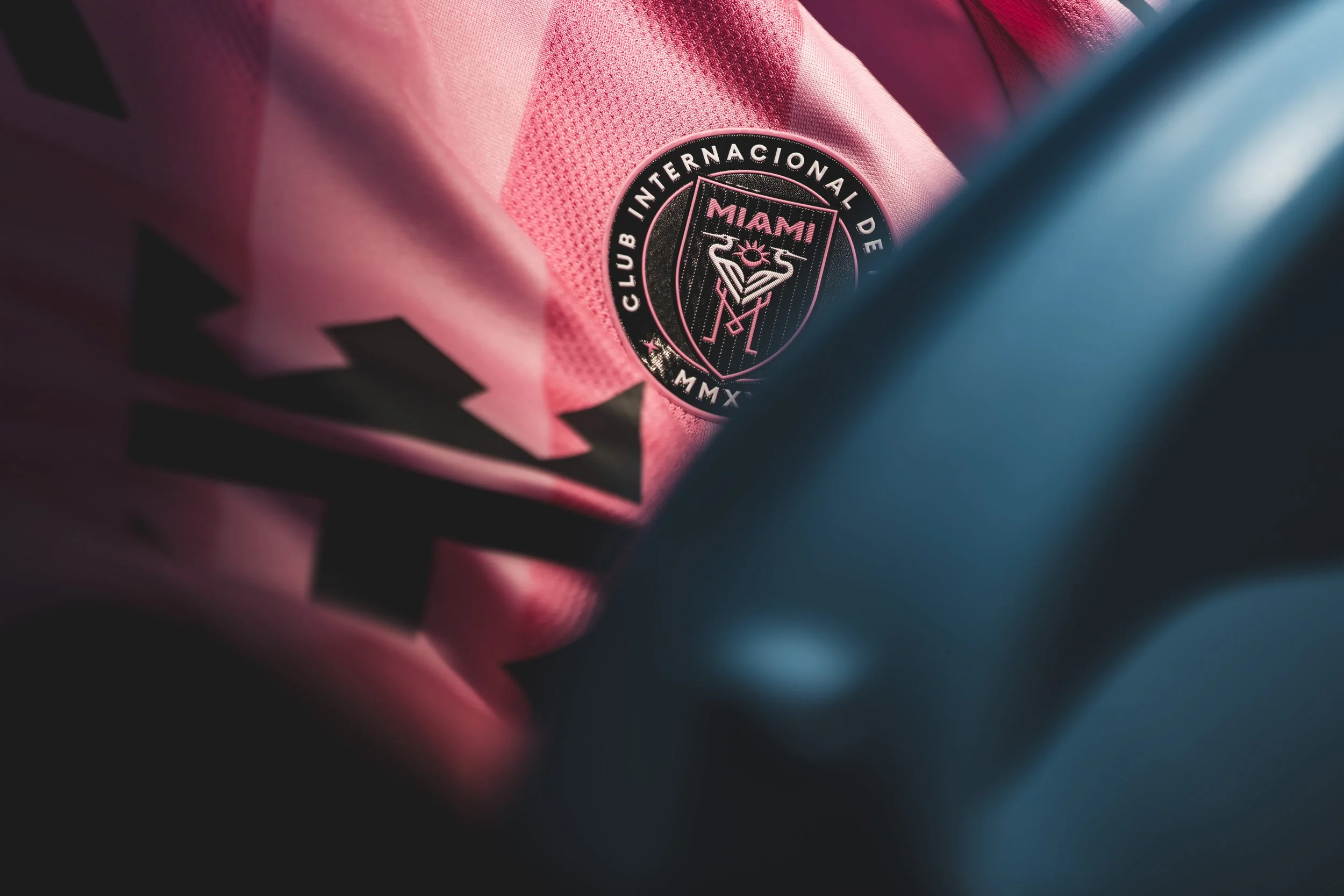Close-up of a pink Miami Soccer Club badge on a pink jersey. The badge has a flamingo with two crossed golf clubs and the text 'Miami Club Internacional De' on a black background.