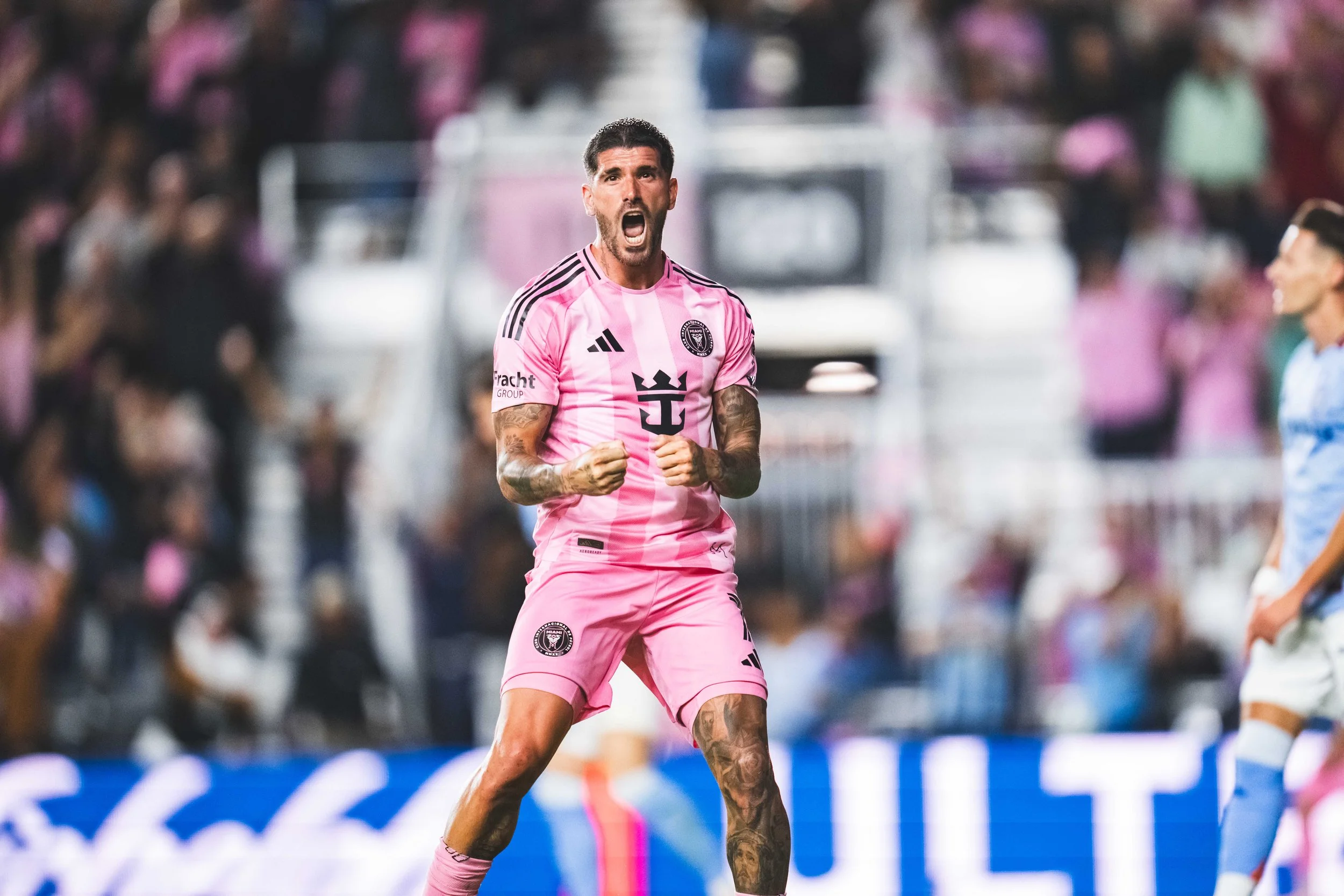 A soccer player in a pink uniform celebrating passionately with clenched fists during a match.