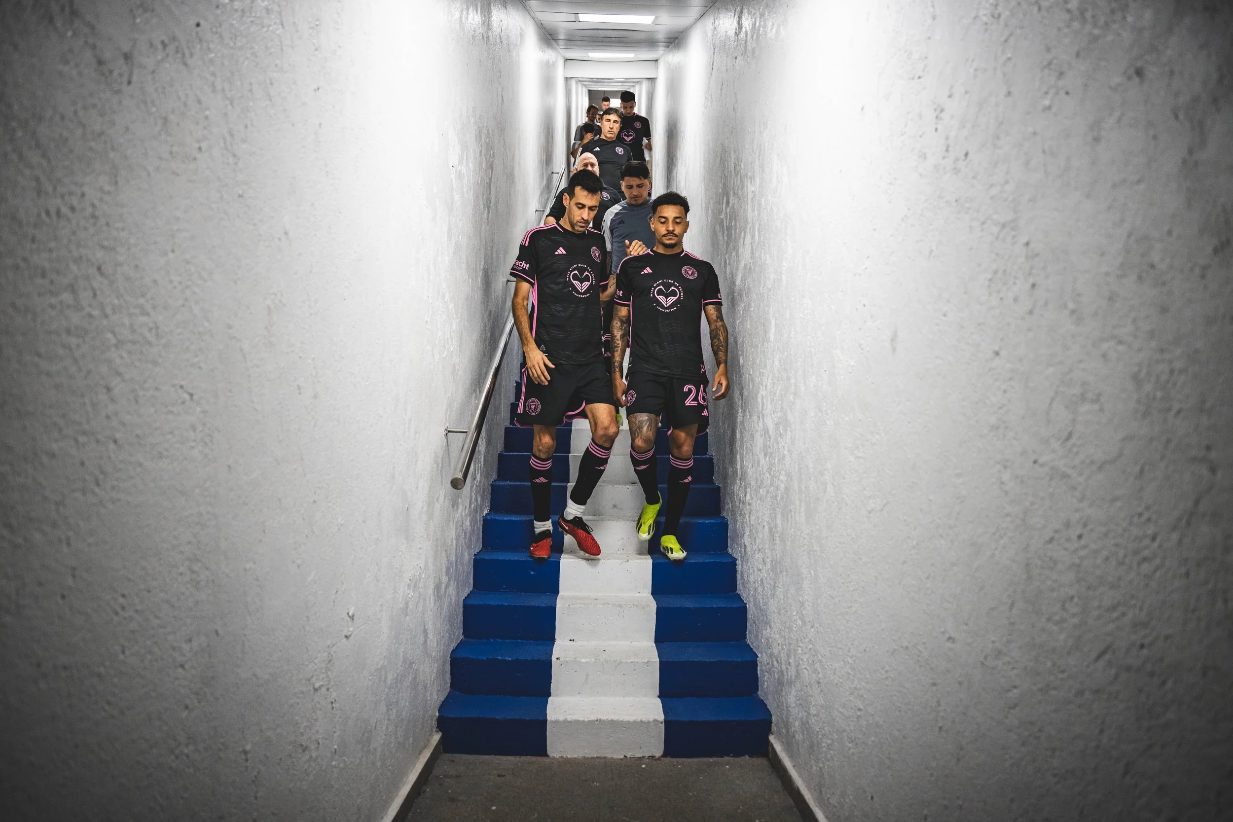 A group of soccer players in black uniforms walking down a narrow staircase in a tunnel.