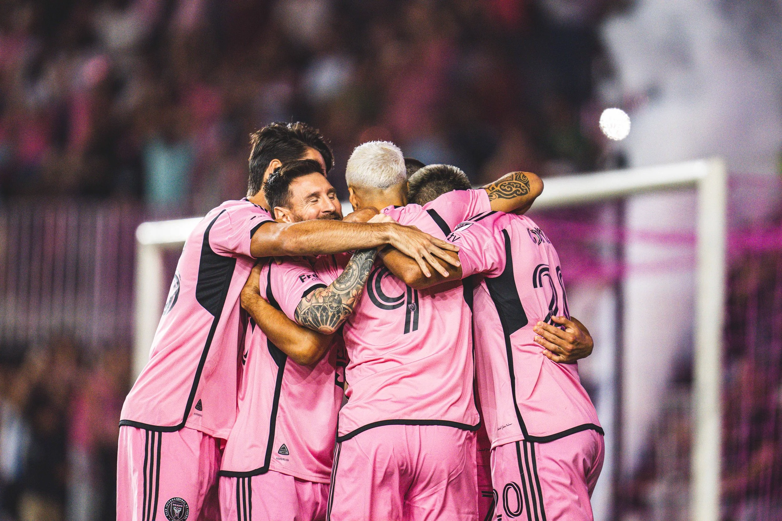 A group of soccer players in pink uniforms hugging and celebrating after a goal or victory on the field.