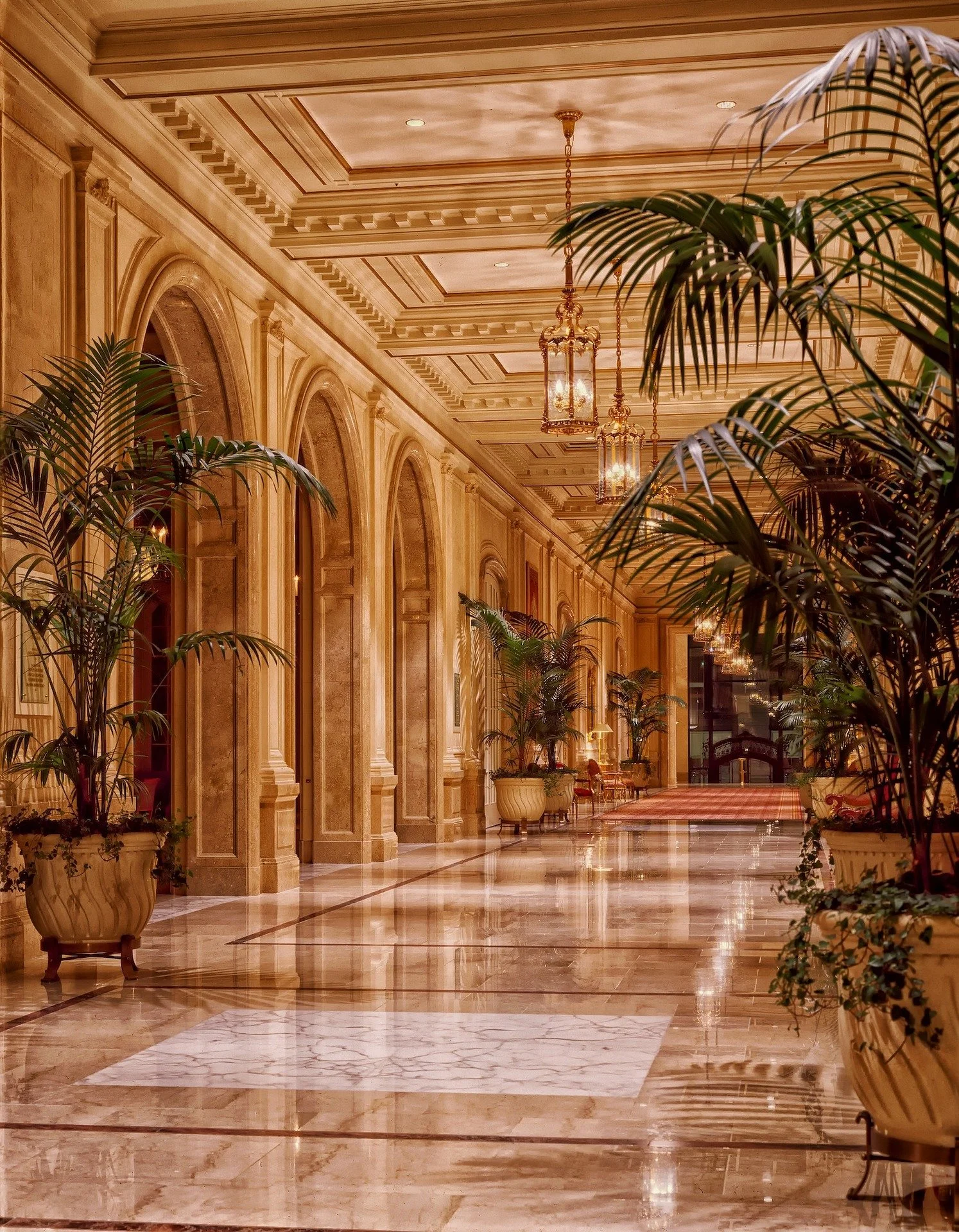 Grand ornate hotel lobby with soaring marble columns, polished floors, and lush tropical palms, showcasing the iconic luxury properties accessible through Carte Blanche Advisors
