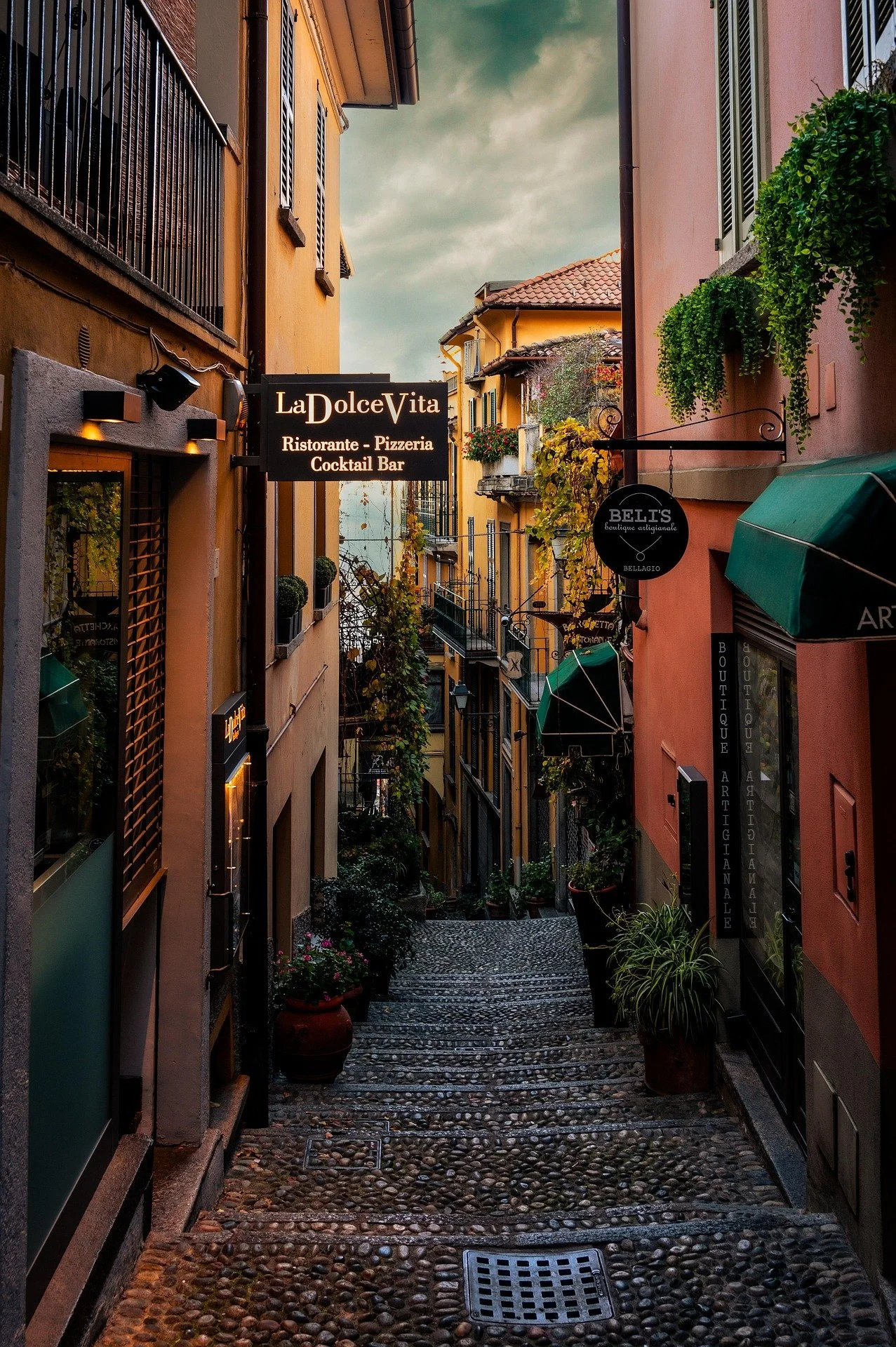 Charming cobblestone alley in Bellagio, Italy lined with colorful boutiques and the La Dolce Vita restaurant, evoking the authentic Italian experiences curated by Carte Blanche Advisors