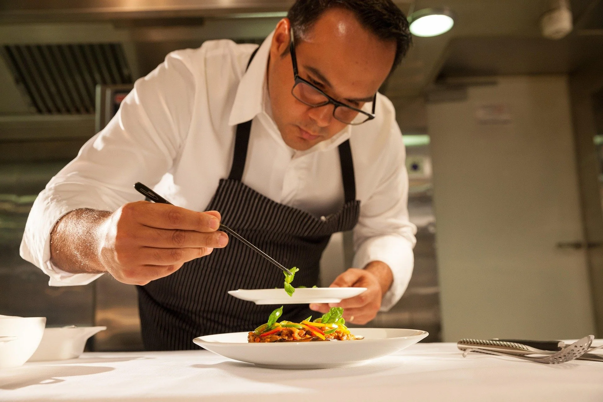 Executive chef meticulously plating a fine dining dish in a professional kitchen, representing world-class culinary experiences curated by Carte Blanche Advisors