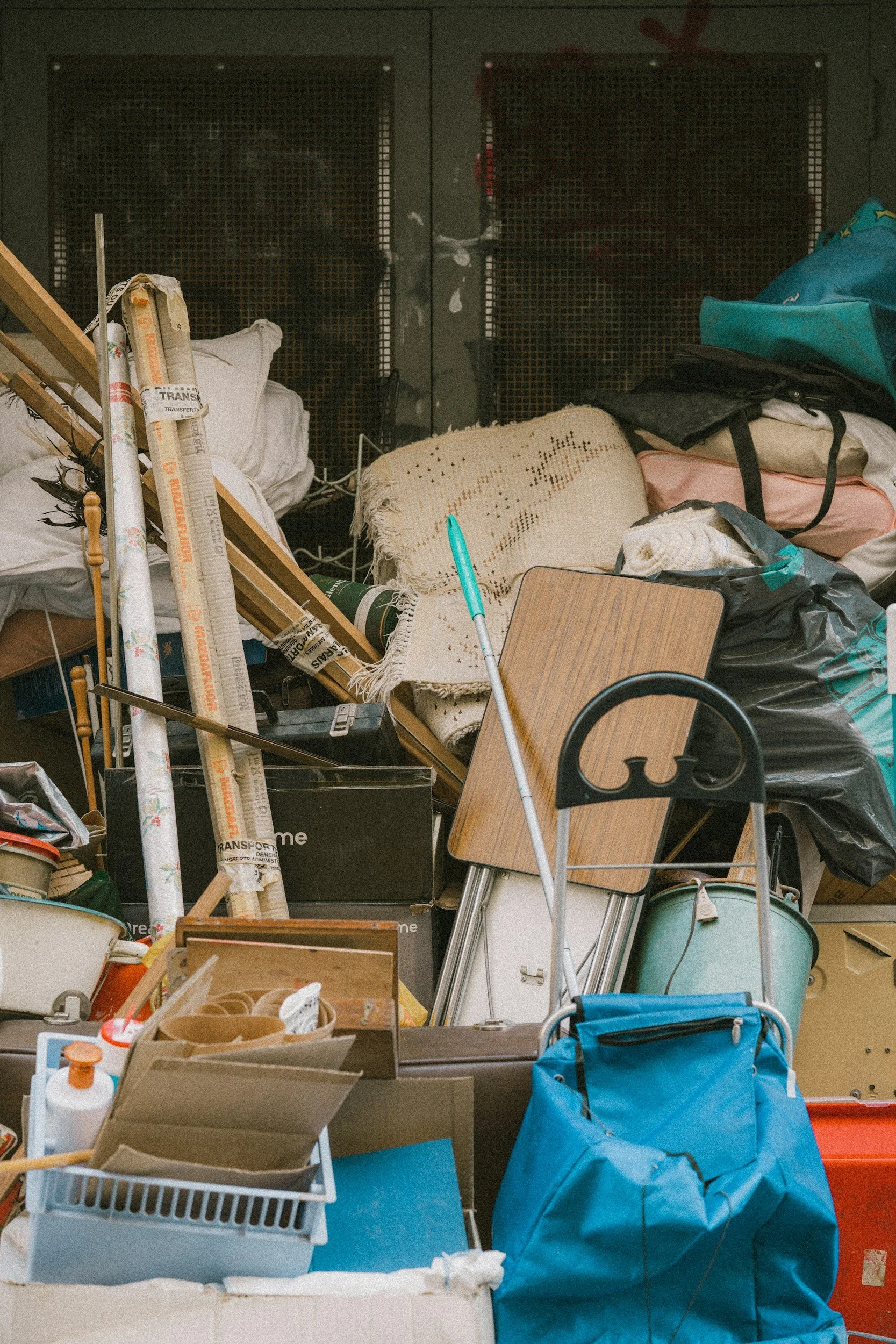 A cluttered pile with various household items, including a broom, wooden table, bags, blankets, cardboard, and miscellaneous objects.