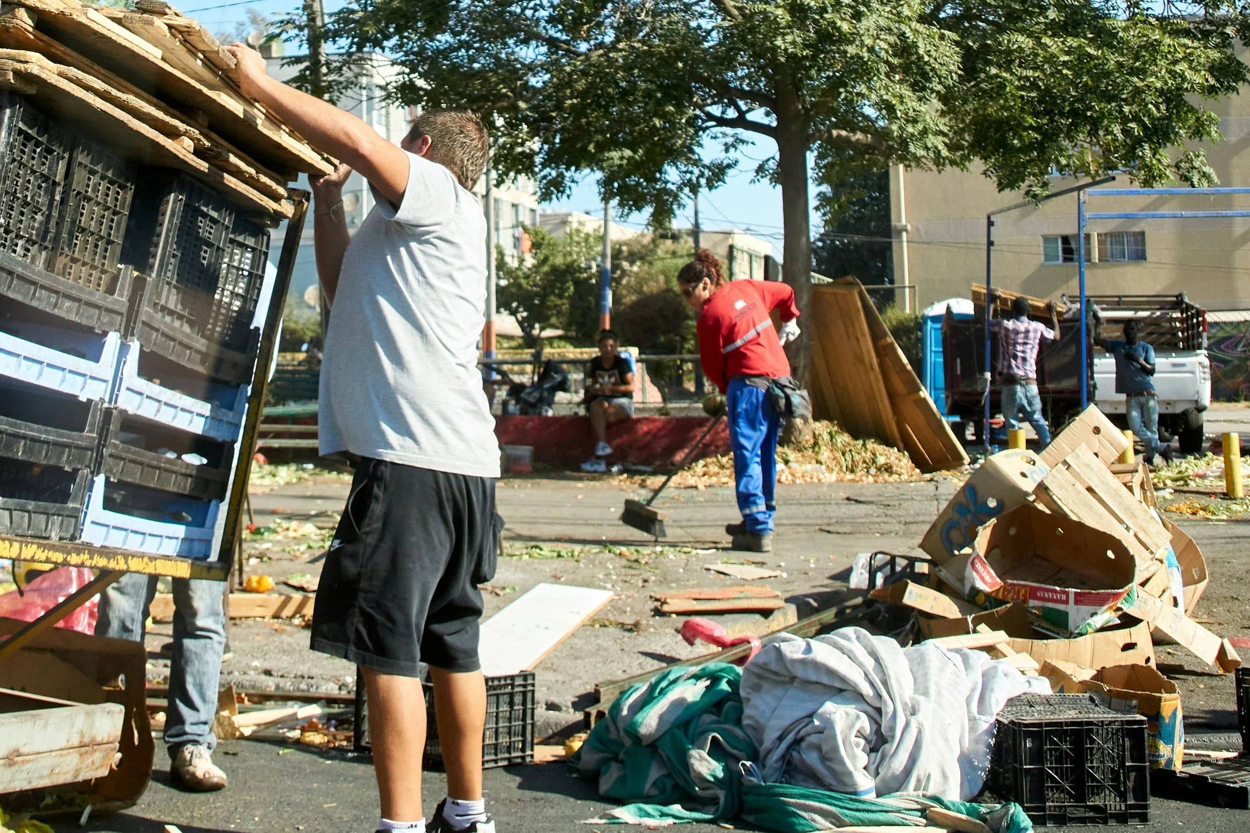 People cleaning up outside in a community trash pickup event, with scattered cardboard boxes and debris on the ground.
