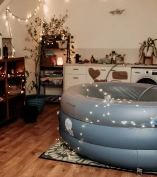 Indoor scene with an inflatable hot tub, string lights, a small table with plants, and a dresser with decor, in a cozy room with wooden flooring.
