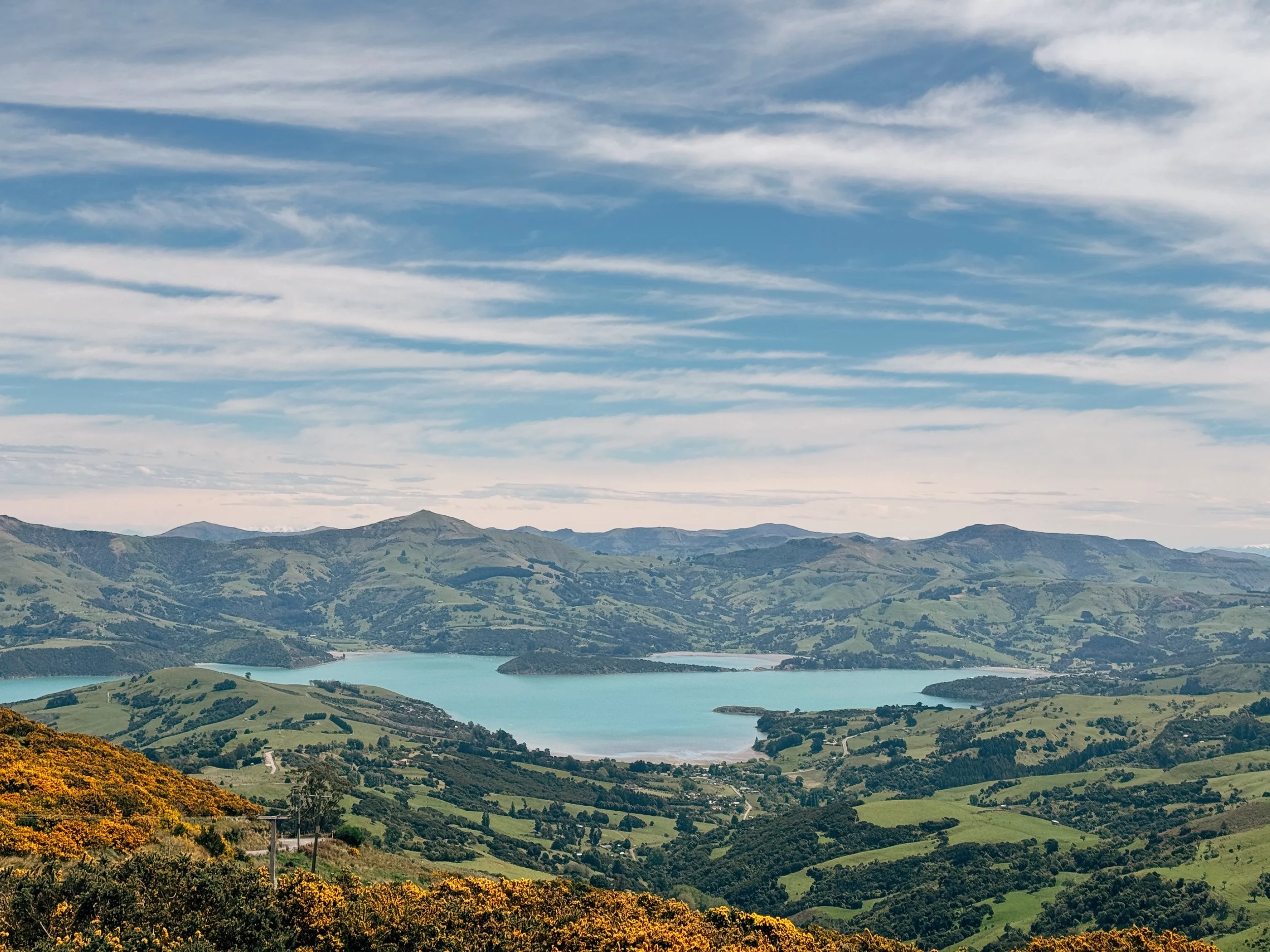 Landscape of rolling green hills surrounding a blue lake with mountains in the background under a partly cloudy sky.