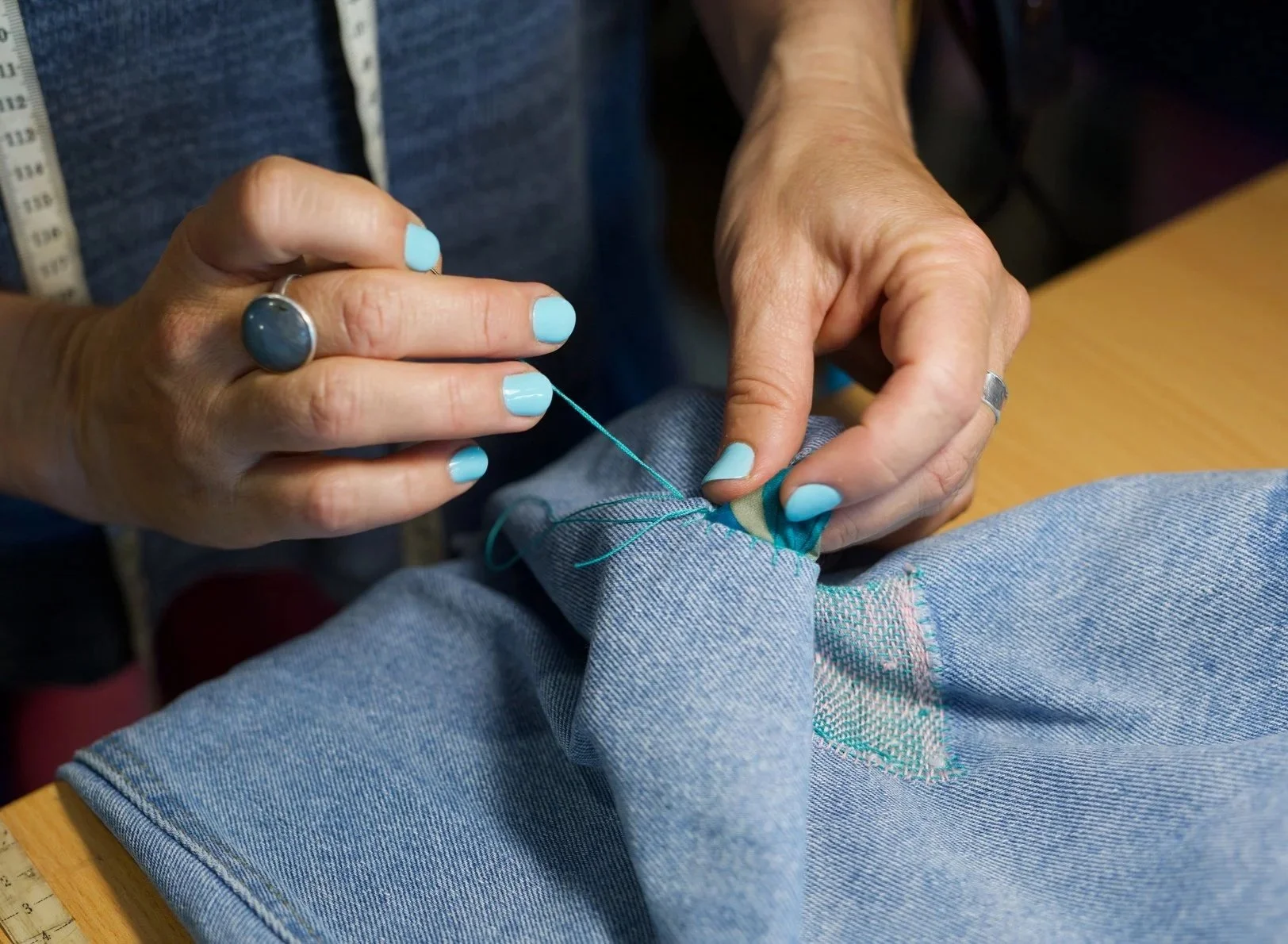 Hand sewing a visible mending patch onto denim jeans using colourful thread.