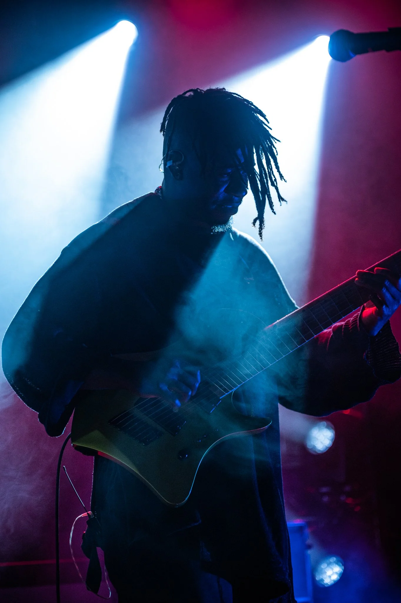 A musician playing an electric guitar on stage with colored stage lighting and fog effects.