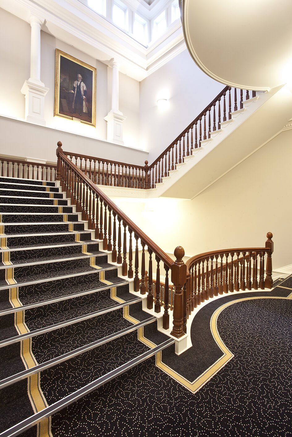 Elegant classical staircase with dark patterned dye-injected carpet, skylight above