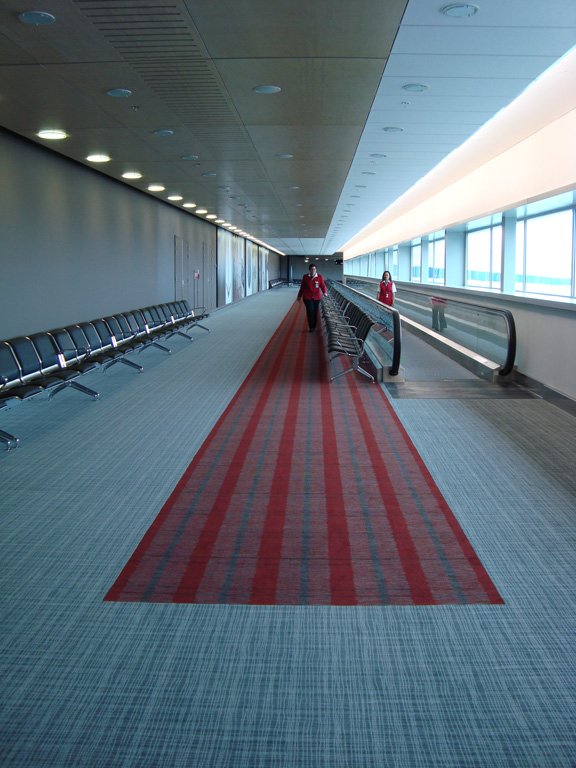 Airport corridor with red-striped runner carpet and staff walking toward camera