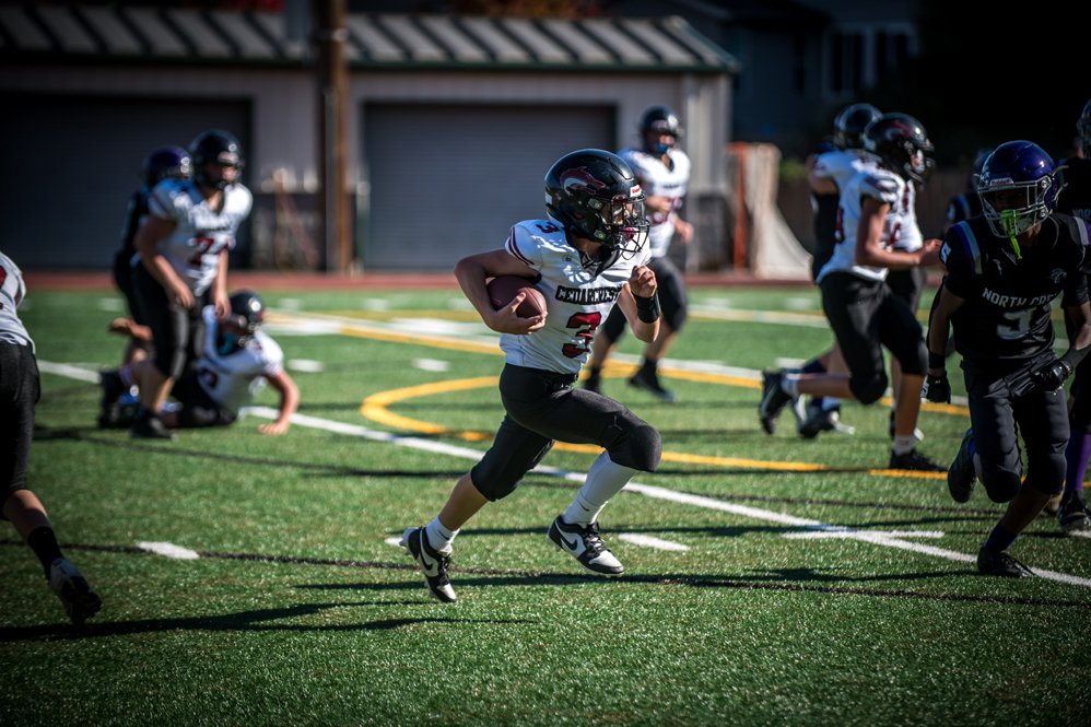 Youth football game on a field with players in black and white jerseys, helmet, and pads