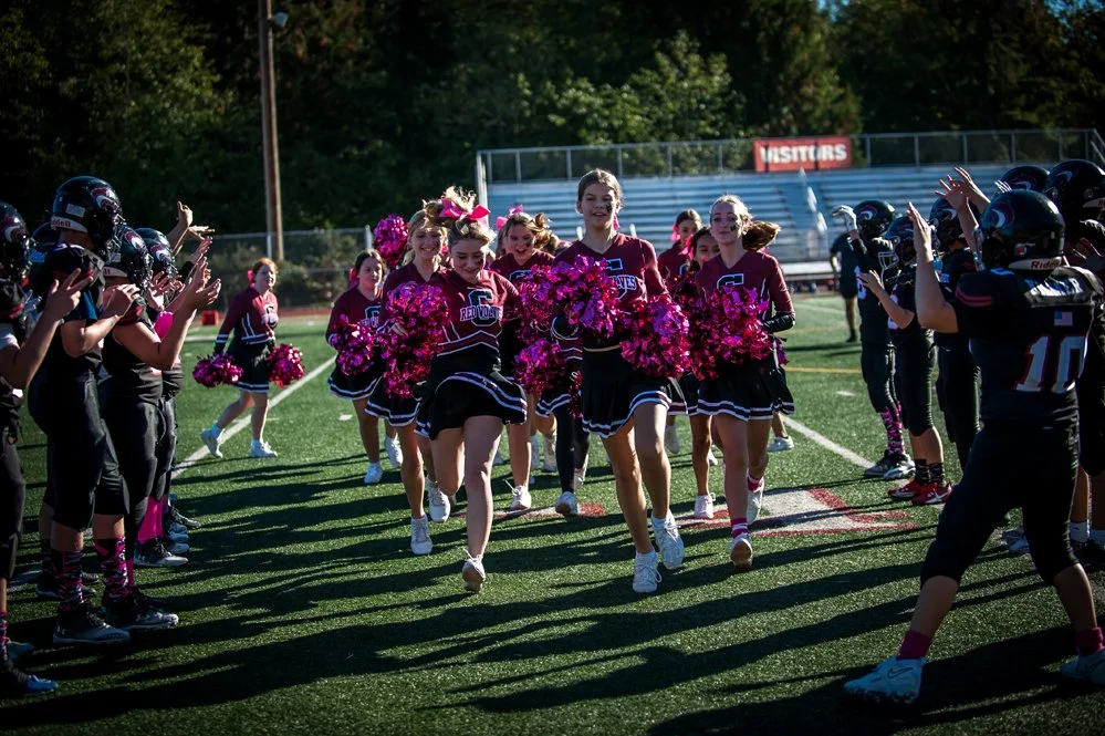 Cheerleaders running onto football field with players on both sides clapping and cheering