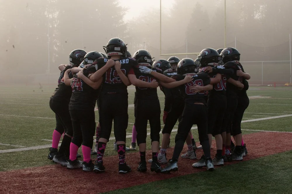 A group of Jr. Red Wolves football players huddle together on a football field.