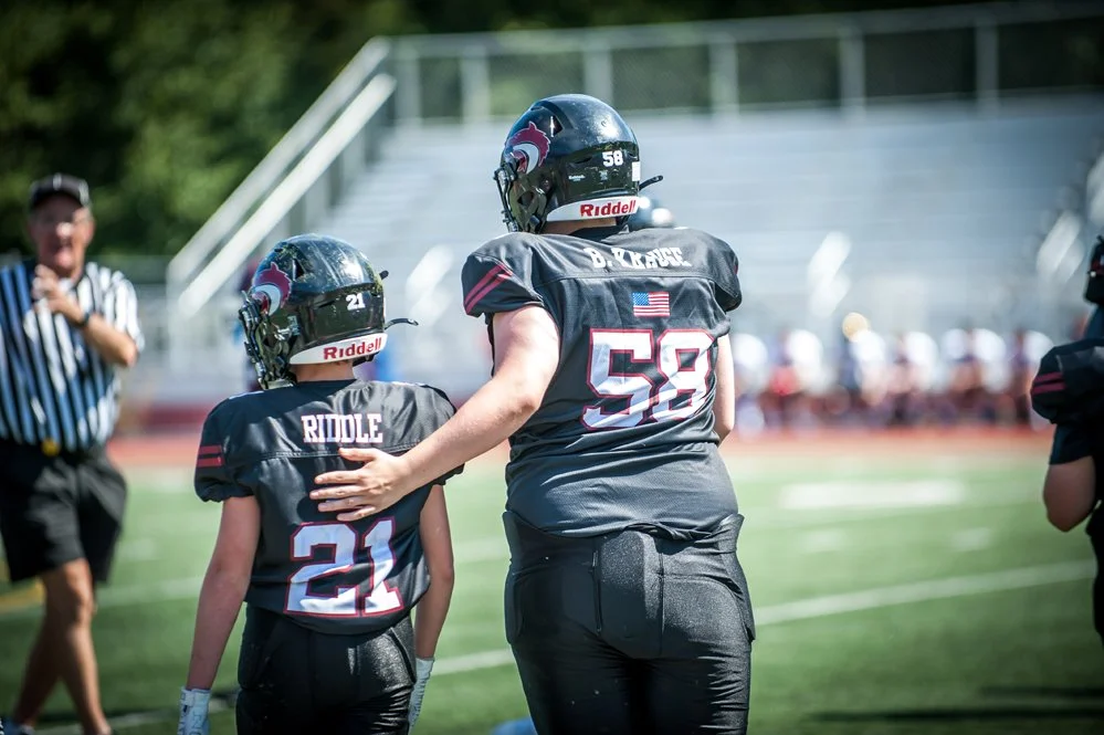 Two football players walking on a football field, with one player placing a hand on the other's shoulder.