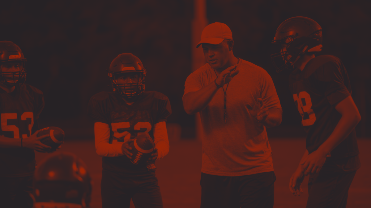 Football coach talking to young football players during practice on the field.