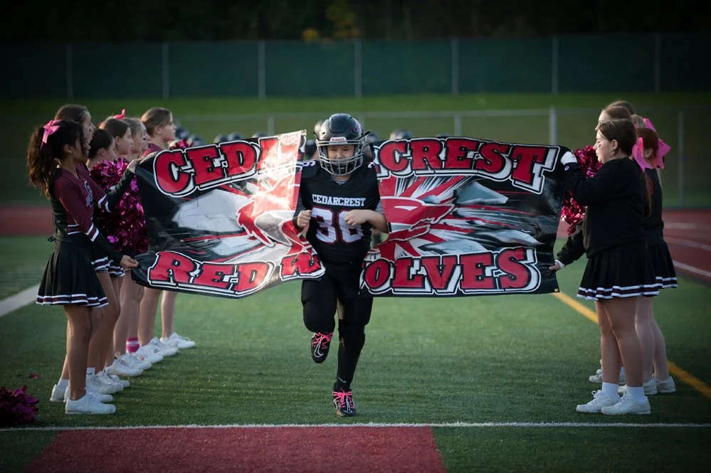 A football player wearing a uniform breaks through a banner held by cheerleaders.
