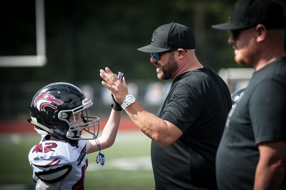 A young football player giving a high five to a coach on the sideline during a game.